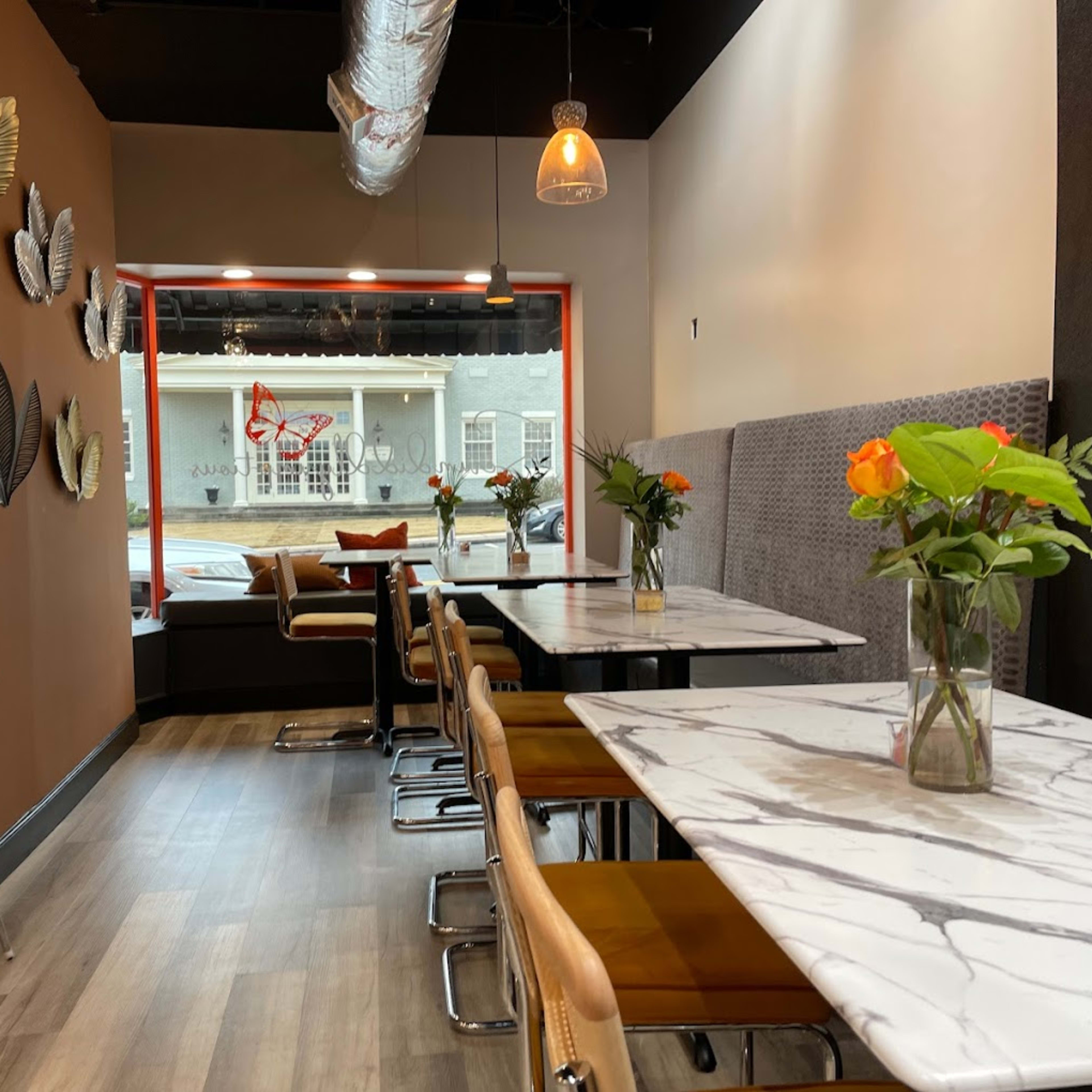 The interior of a modern cafe features marble-topped tables with floral centerpieces, surrounded by brown and orange seating elements.