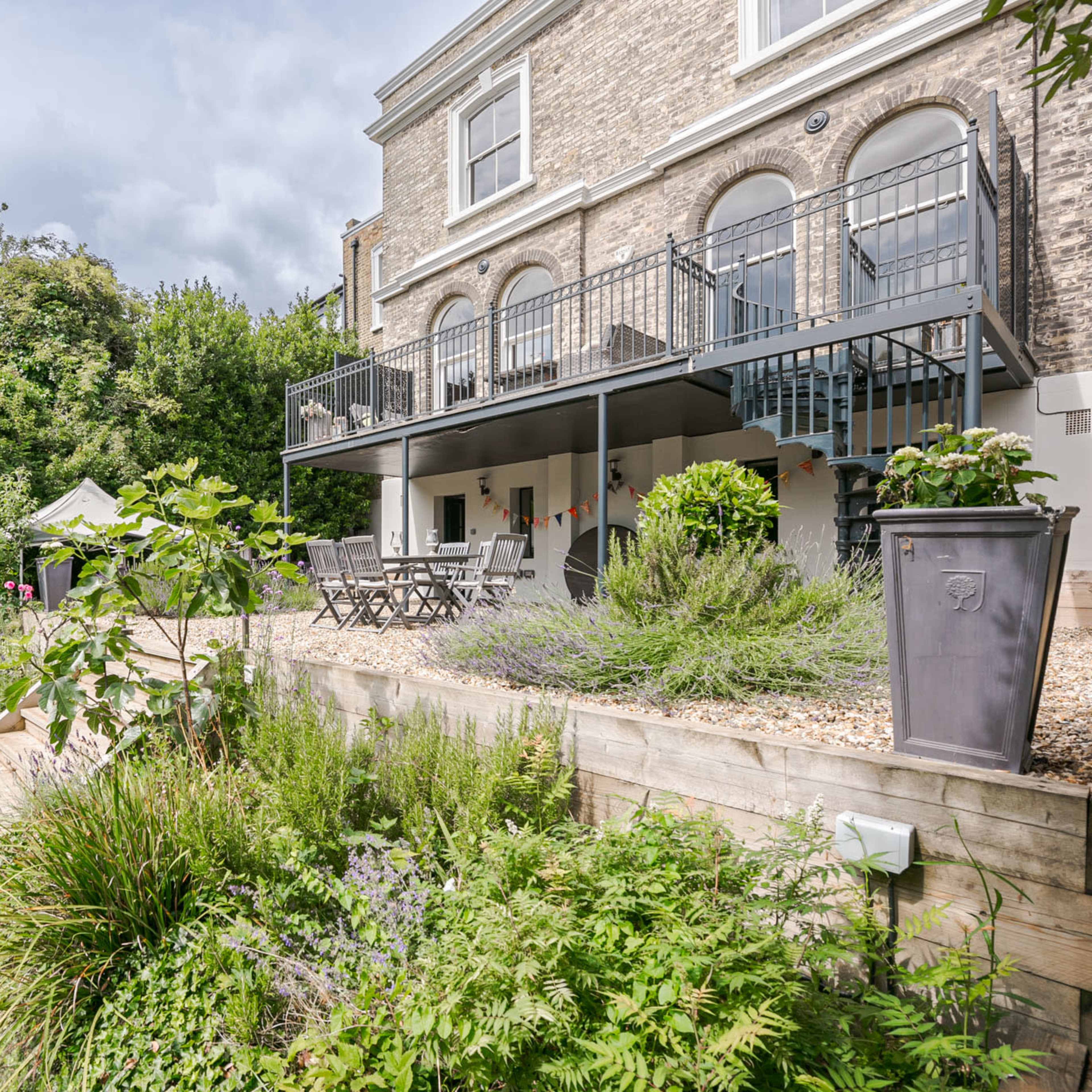 A brick building with large arched windows overlooks a landscaped garden featuring a wooden deck and seating area.
