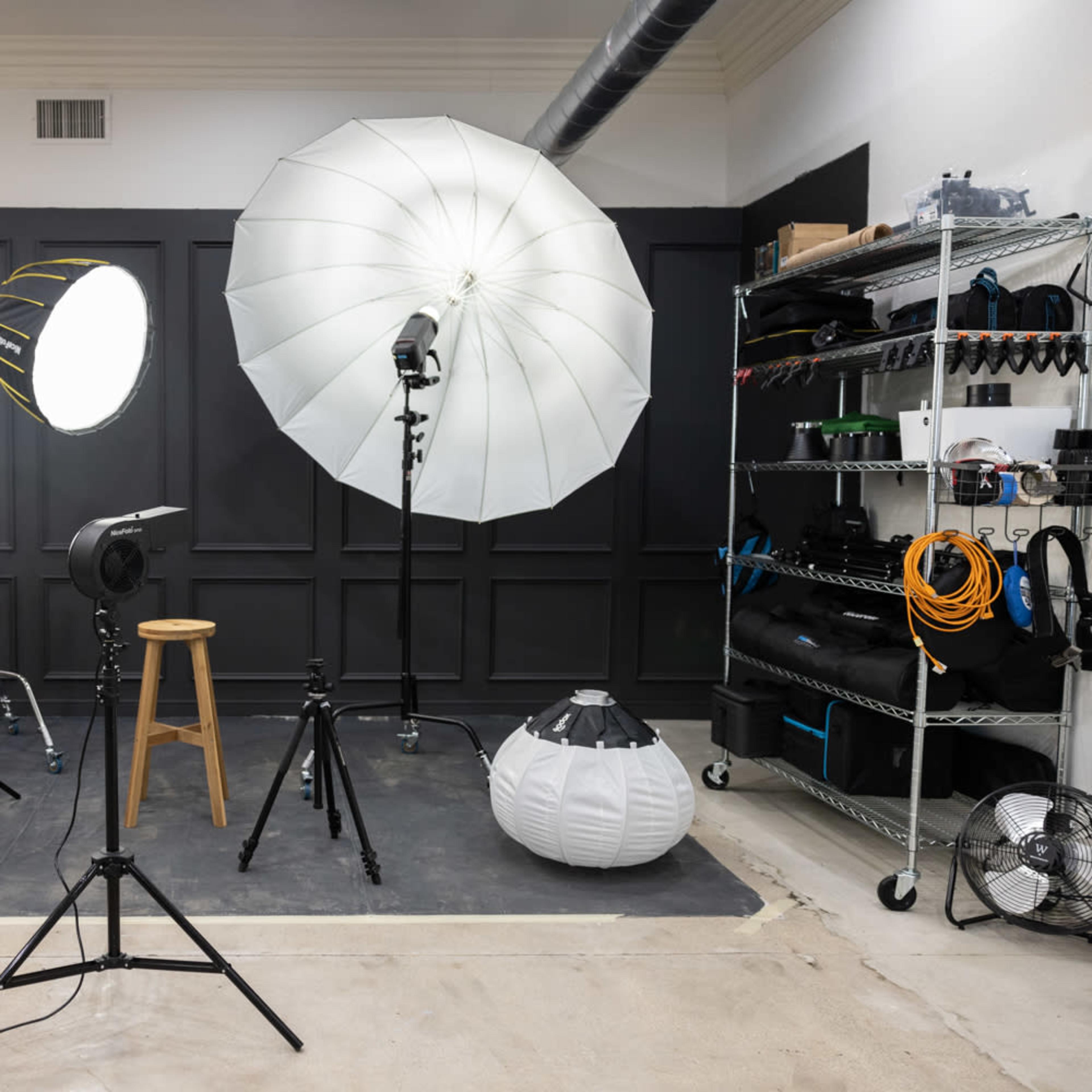 A photography studio setup with various lighting equipment, a stool, and backdrops arranged against a black wall.
