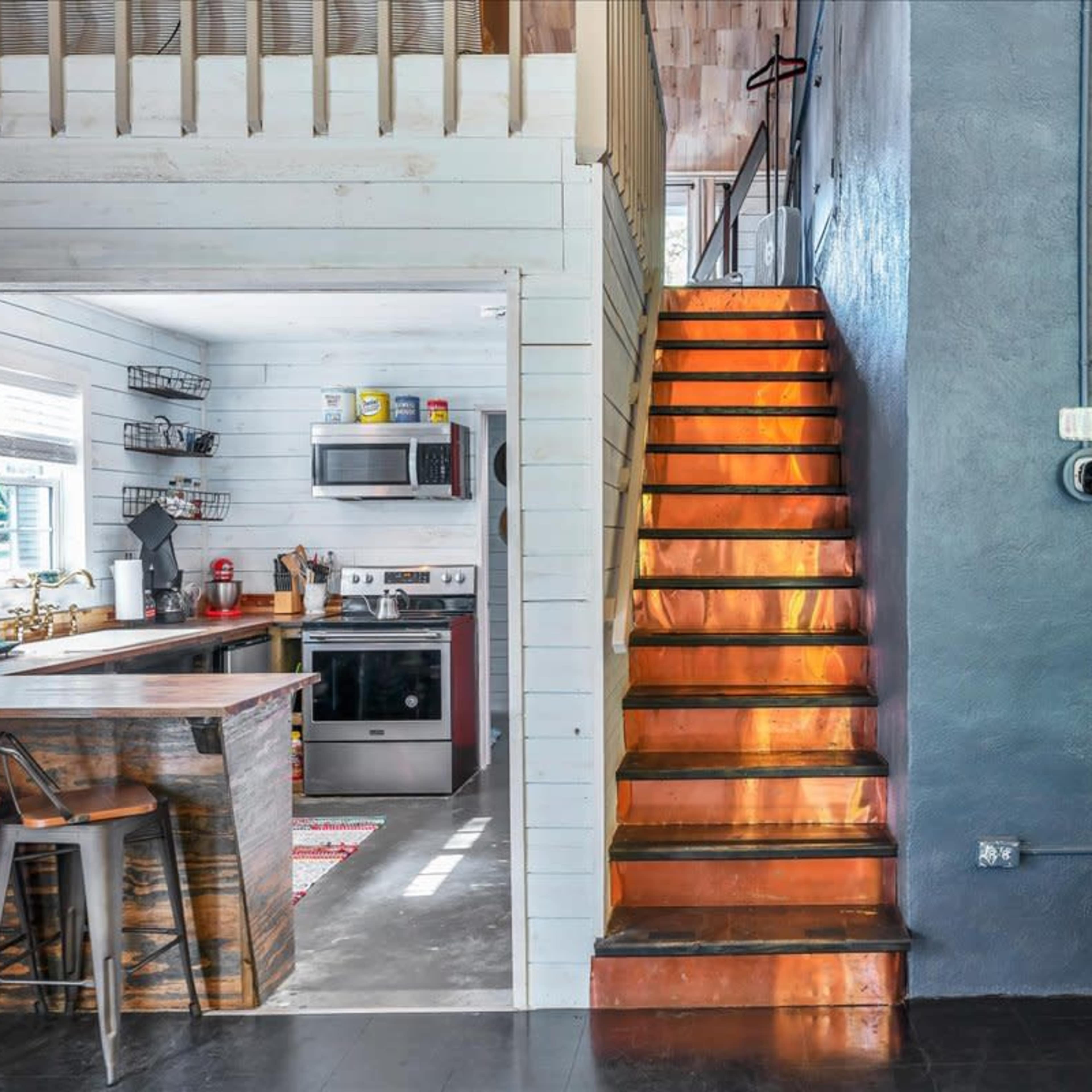 A modern living space with a view of a kitchen to the left and a staircase leading to an upper level on the right.