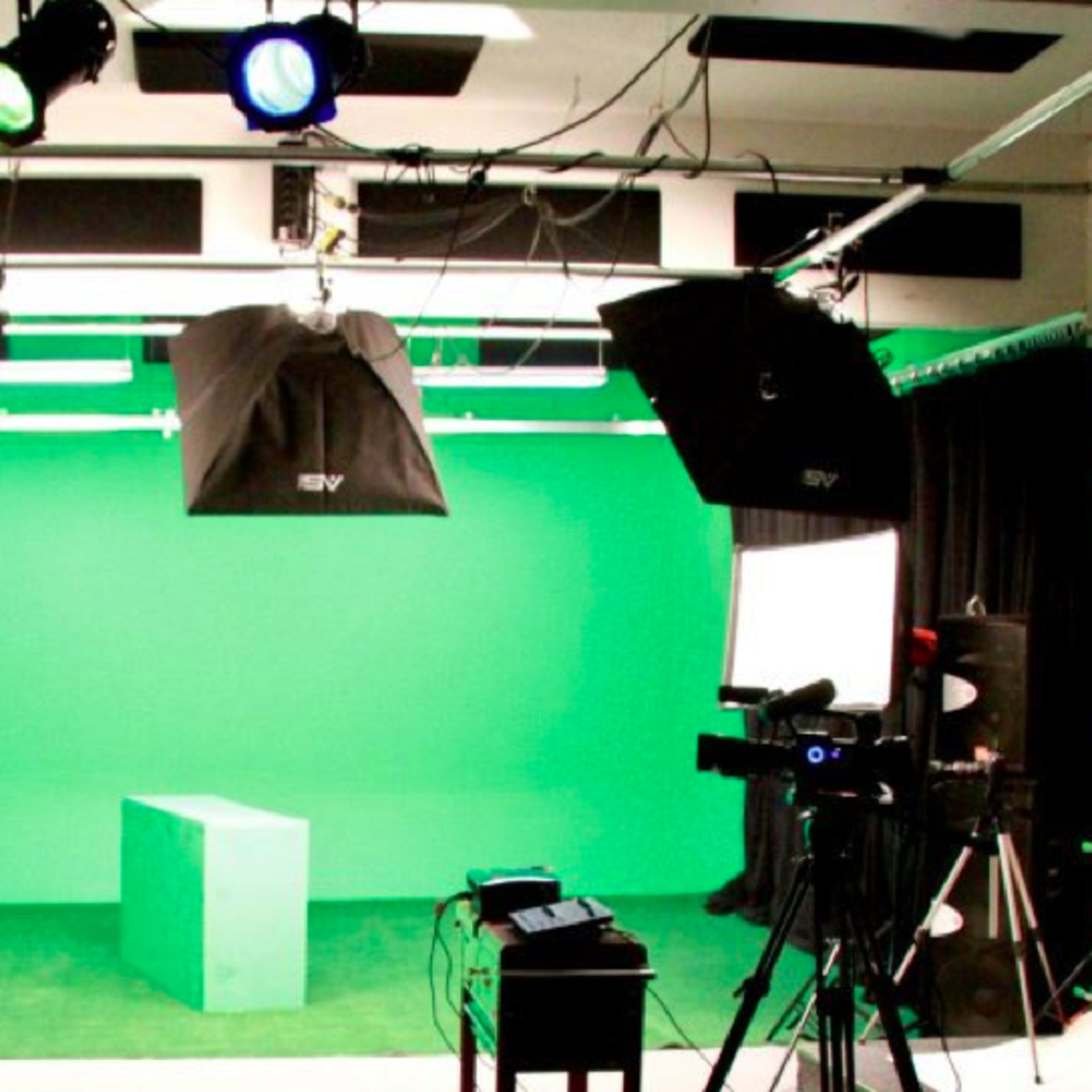 A green screen studio setup with lighting, a green box in the center, and various cameras and equipment arranged around the space.