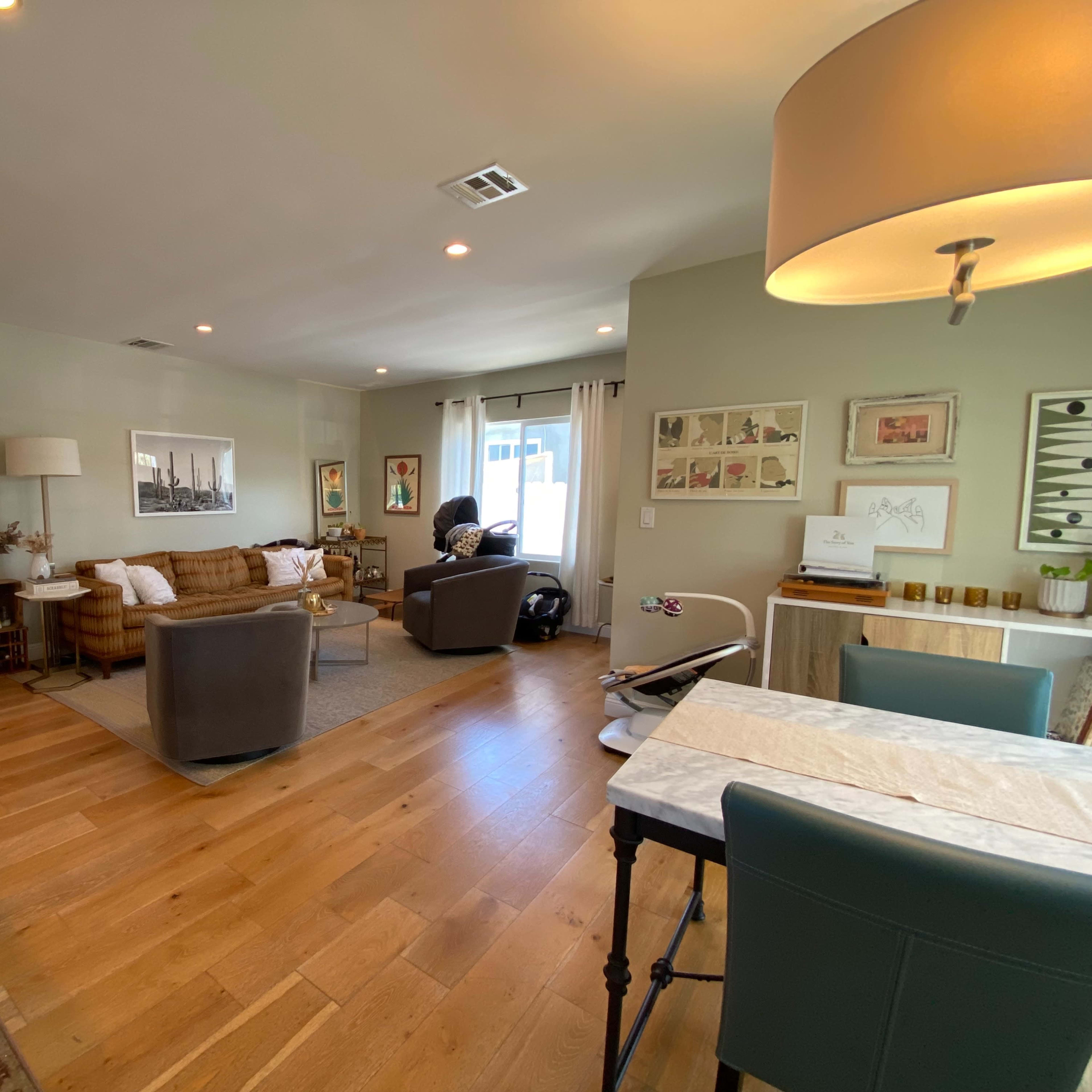 A spacious living area featuring a mix of seating, artwork on the walls, and a dining table with chairs.