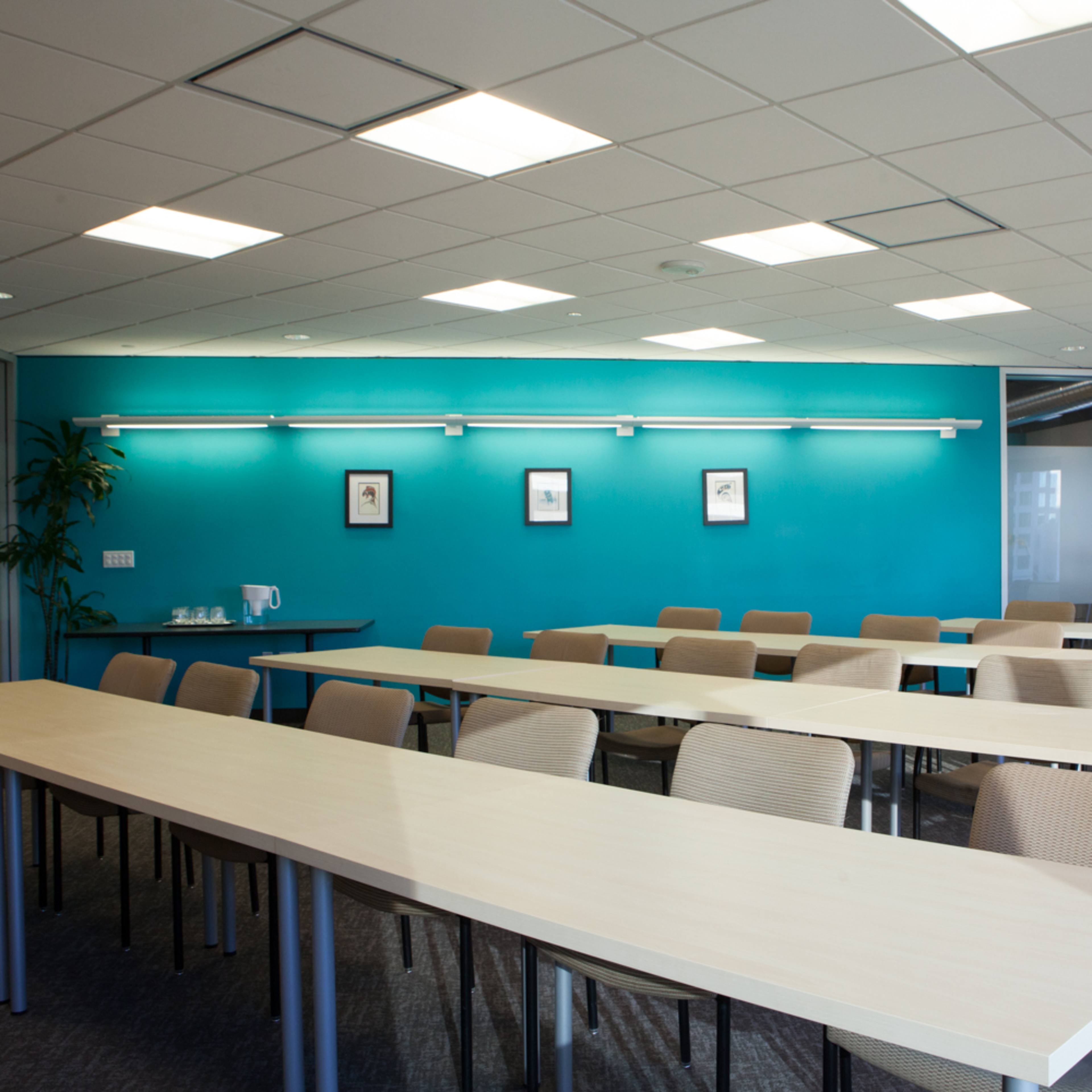 A modern conference room with long tables arranged in rows, accented by a turquoise wall and equipped with soft lighting.