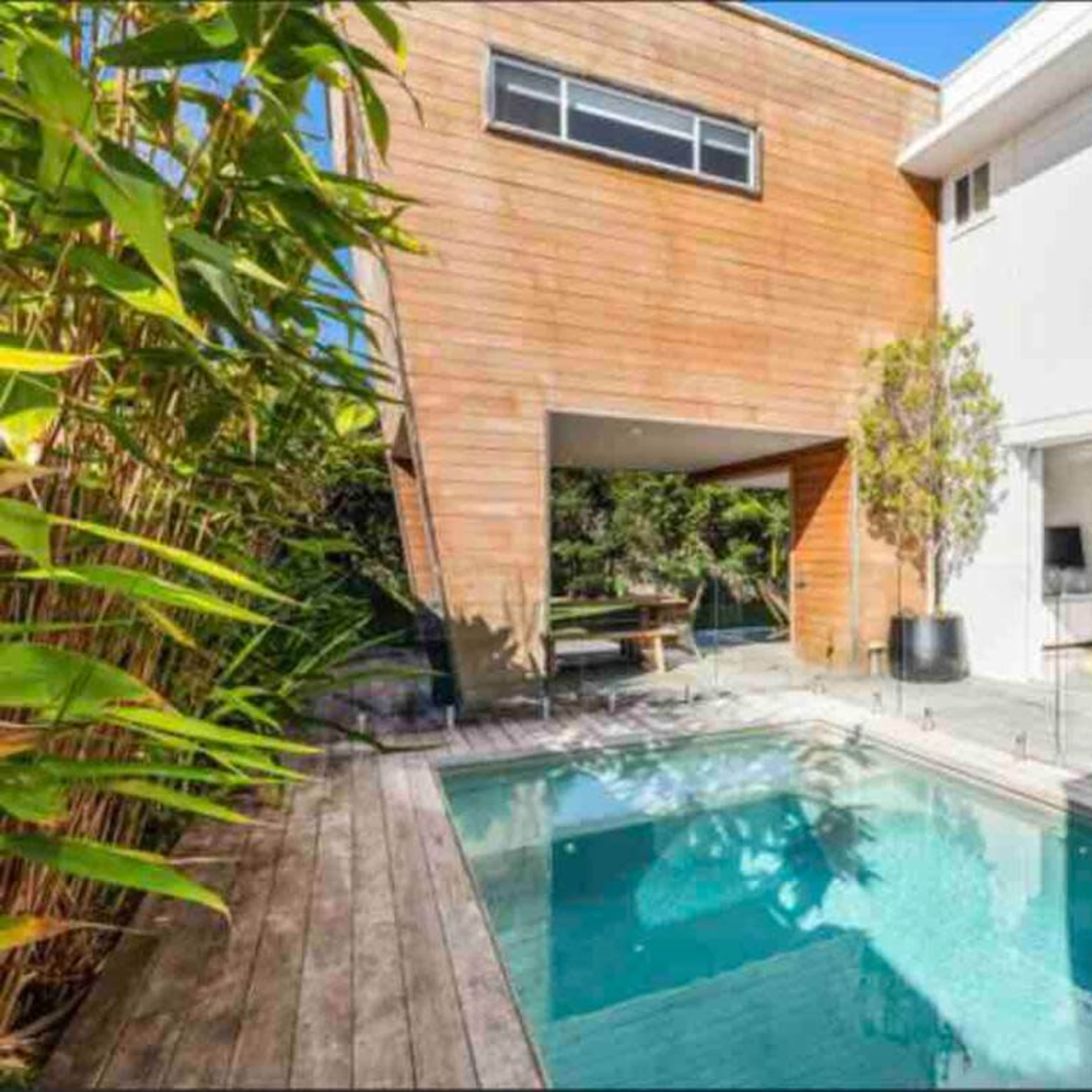 A modern home with a wooden exterior, a swimming pool, and a patio area surrounded by greenery.