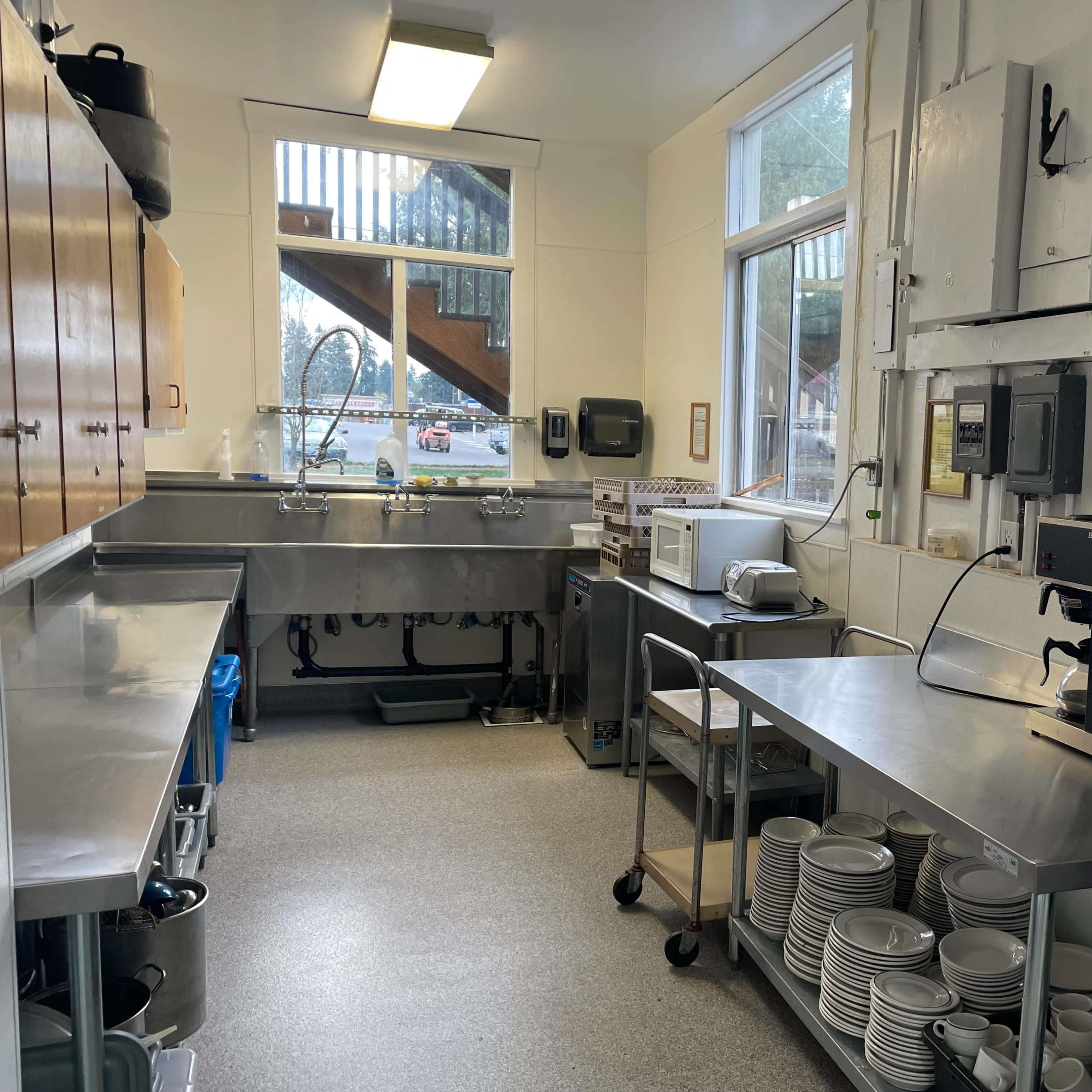 A kitchen with stainless steel countertops, a sink area, kitchen appliances, and shelves with dishes.