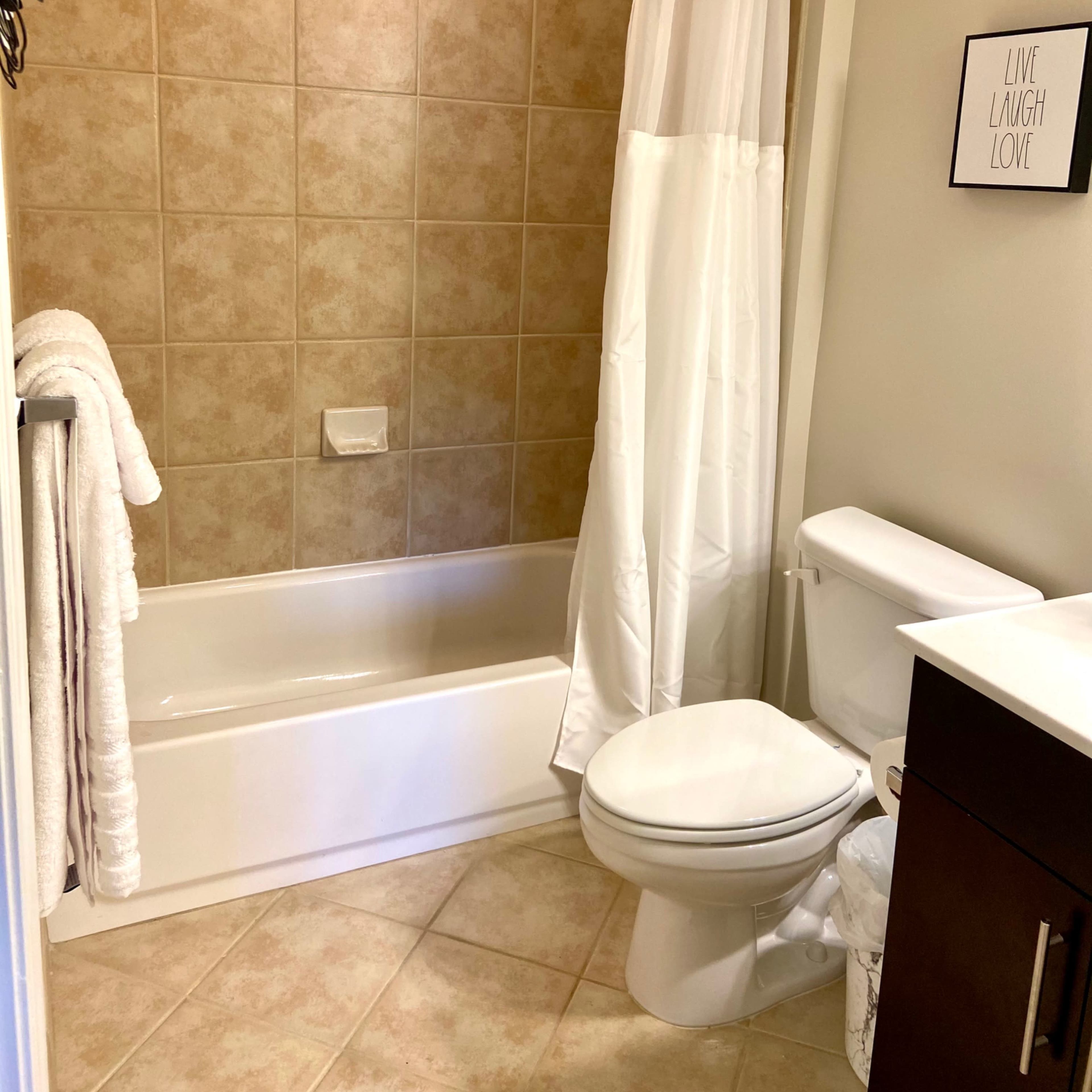 A bathroom featuring a tub with a shower curtain, a toilet, a sink with a mirrored cabinet, and tiled walls.