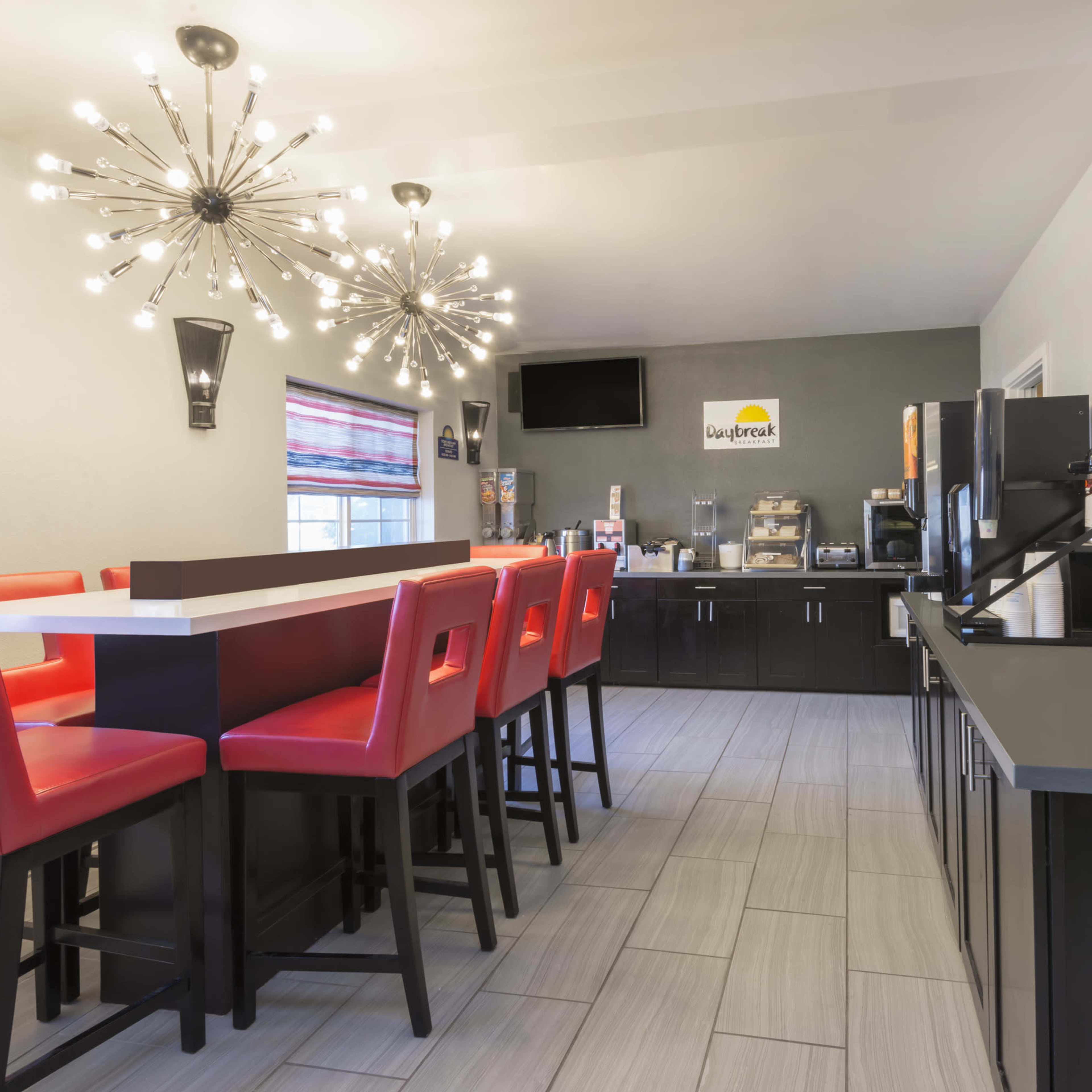 A modern dining area with high tables and red chairs, a dark cabinetry counter, and decorative light fixtures.