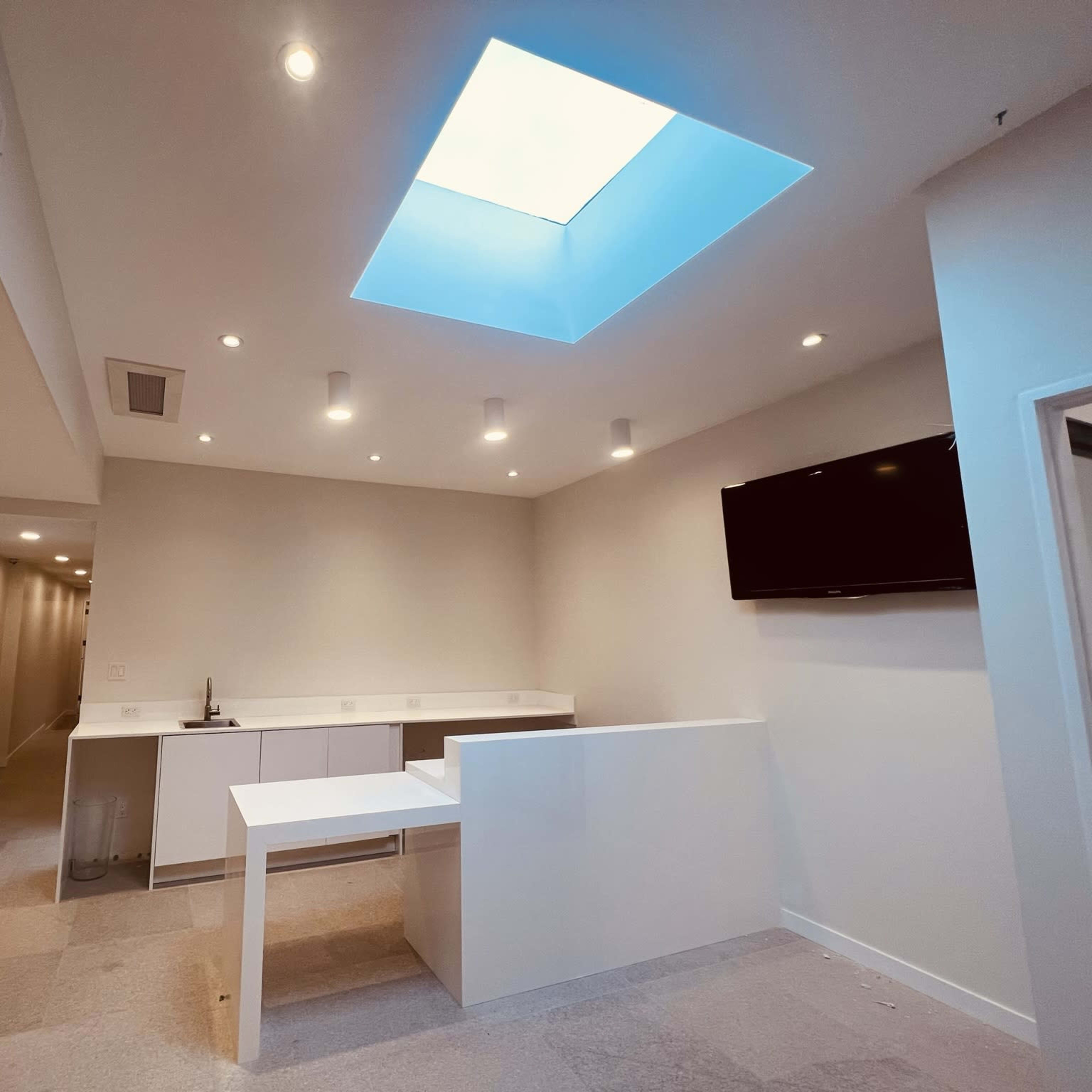 A modern, minimalist room featuring a skylight, a white counter, and a television mounted on the wall.