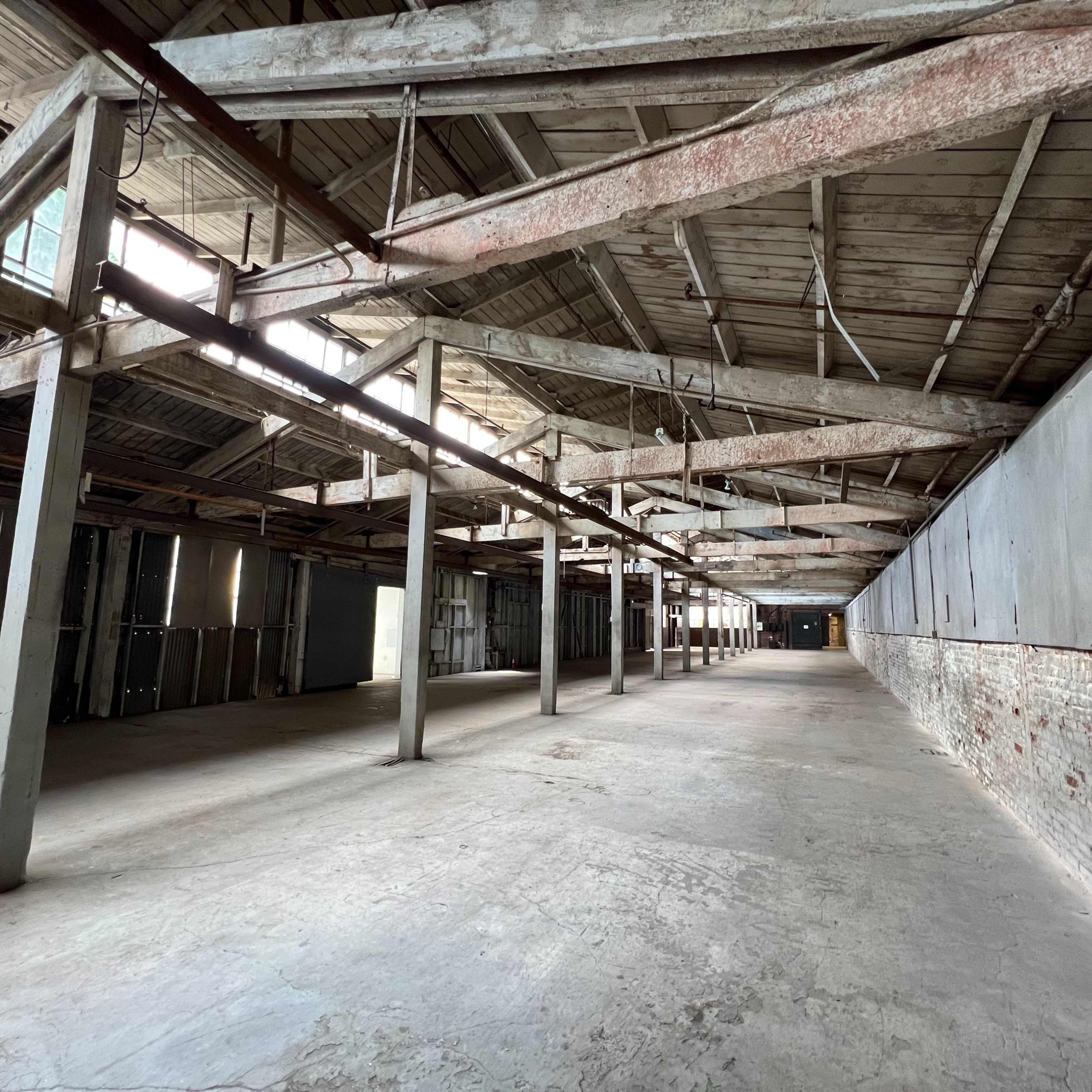 The interior of an empty, dilapidated warehouse with exposed beams and concrete flooring.