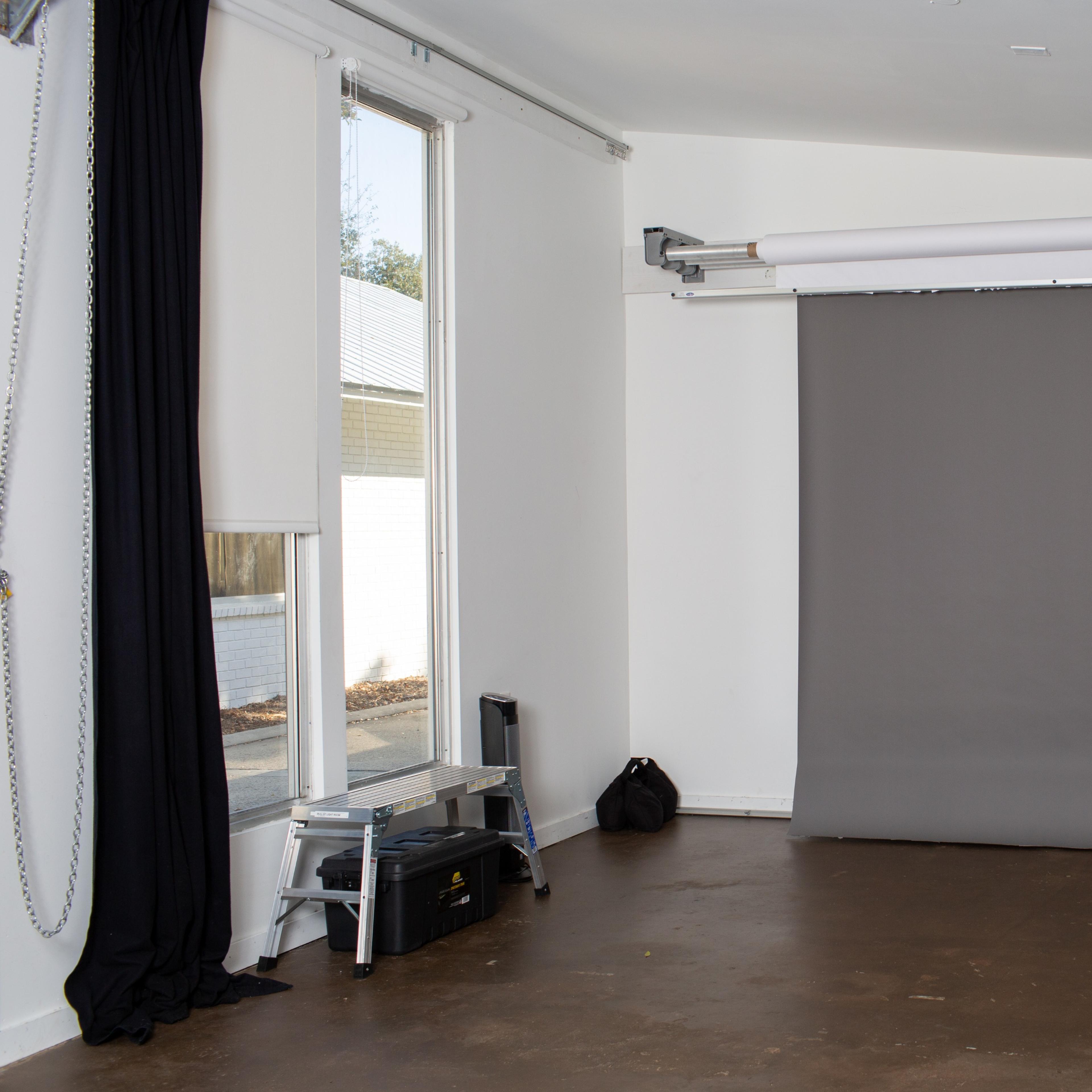 A photography studio with a gray backdrop, large windows, and minimal furnishings.
