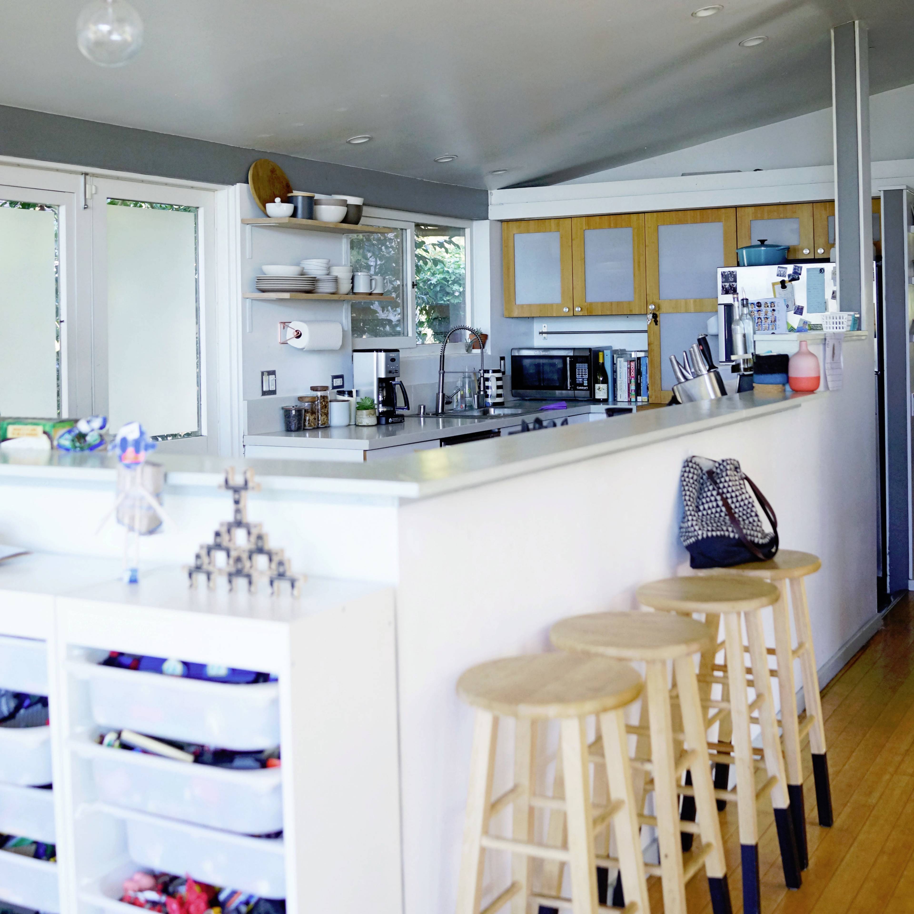 A modern kitchen features a clean design with a central island, bar stools, and shelves displaying dishware and utensils.