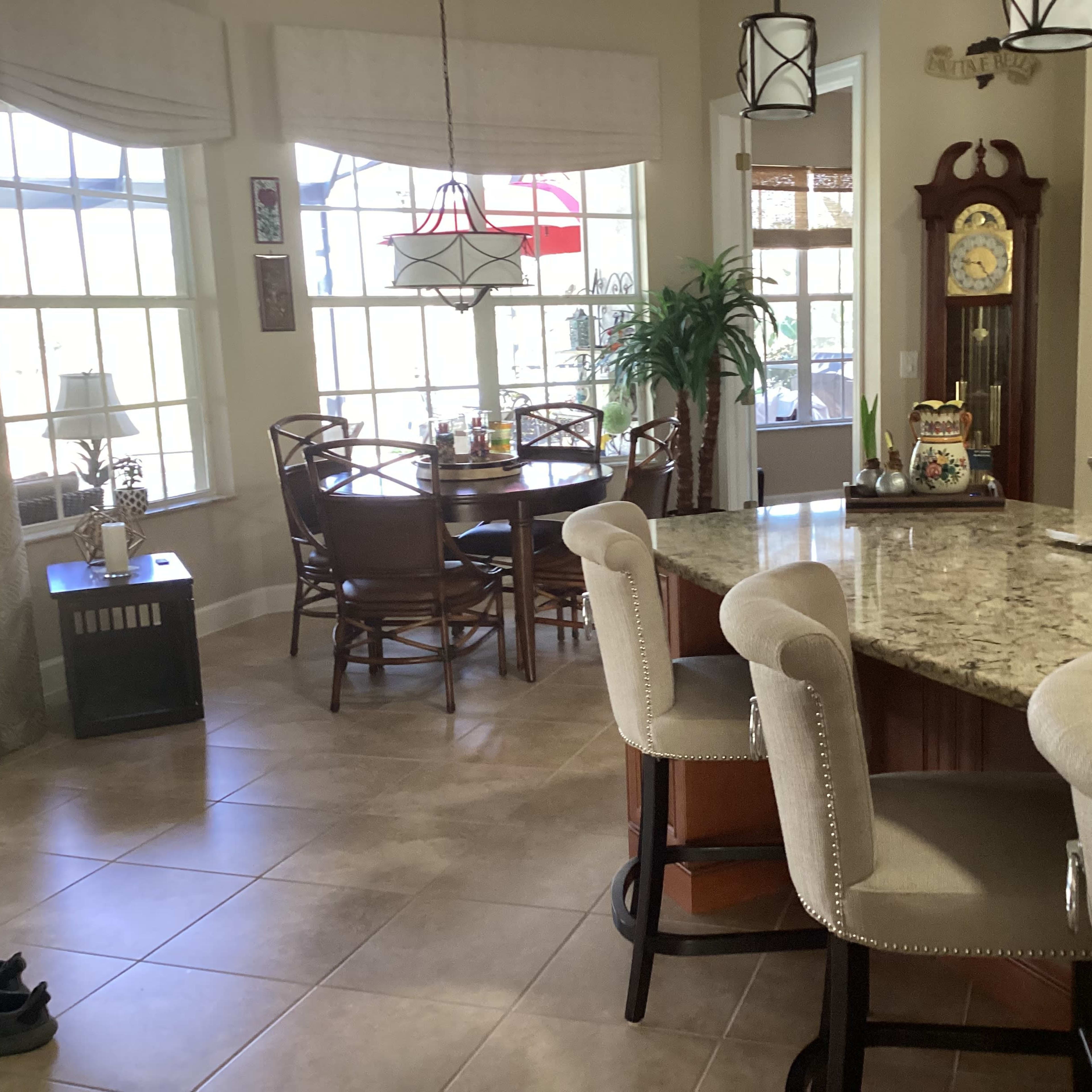 A kitchen area with a granite countertop, bar seating, and dining space filled with natural light from large windows.