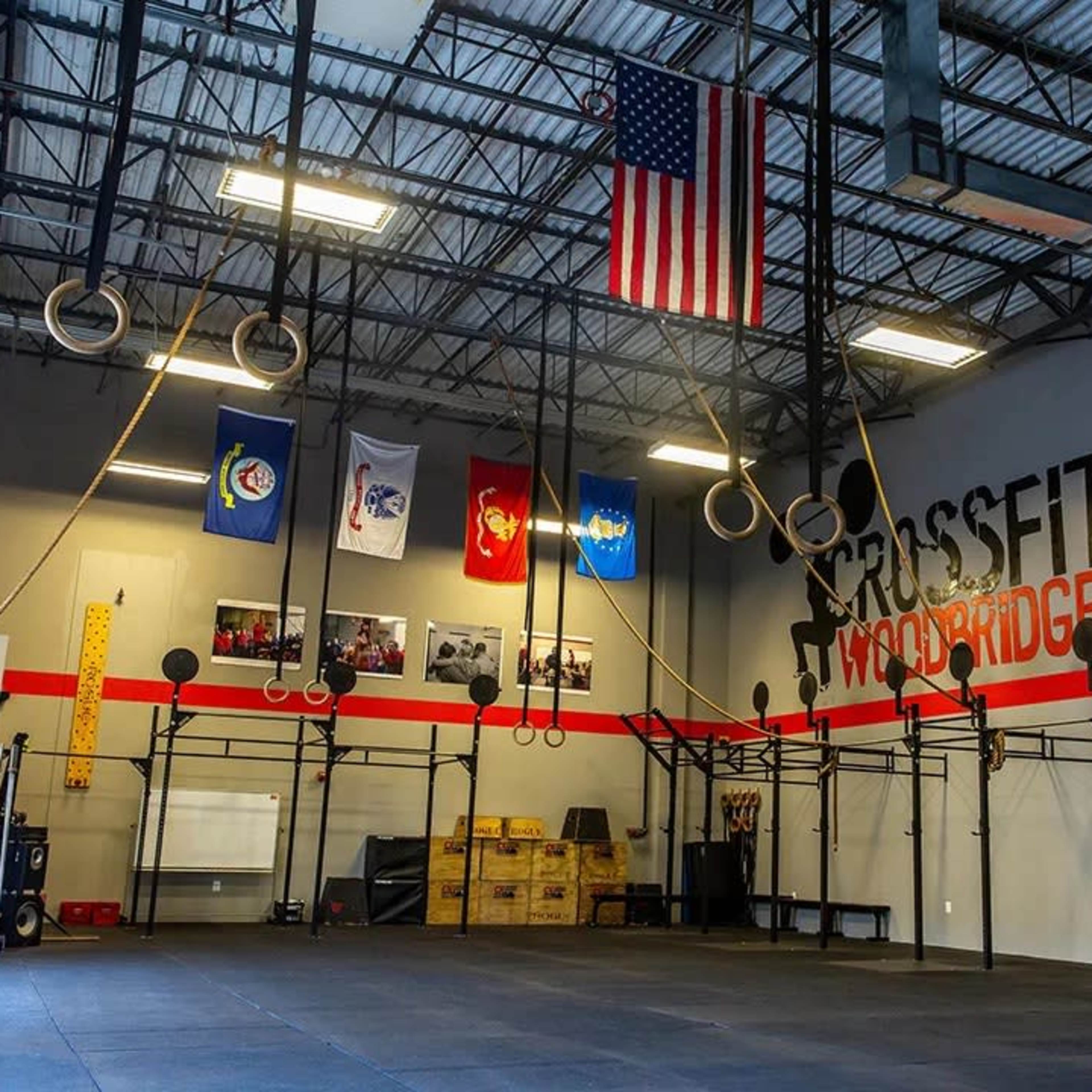 The interior of a CrossFit gym with gymnastic rings hanging from the ceiling and various flags displayed on the walls.
