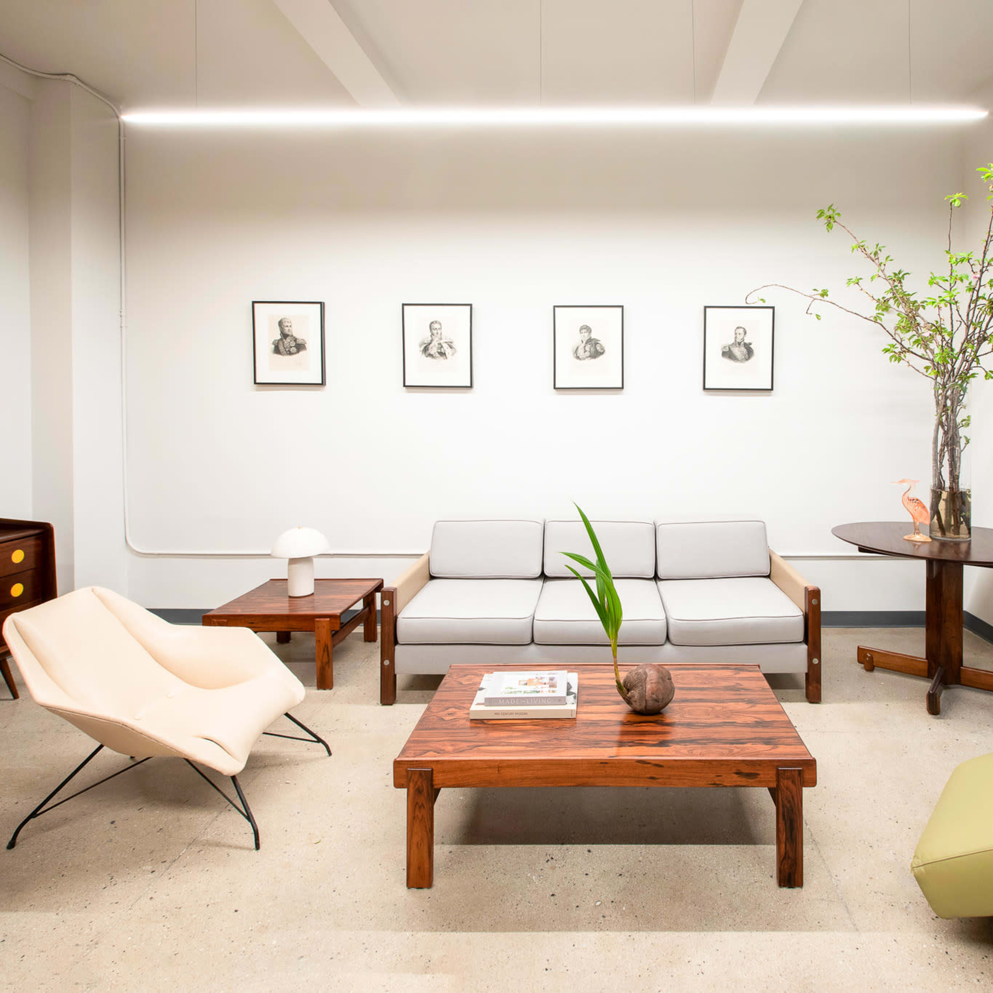 A modern interior features a gray couch, wooden coffee table, and various chairs, with framed artworks and a plant accentuating the space.