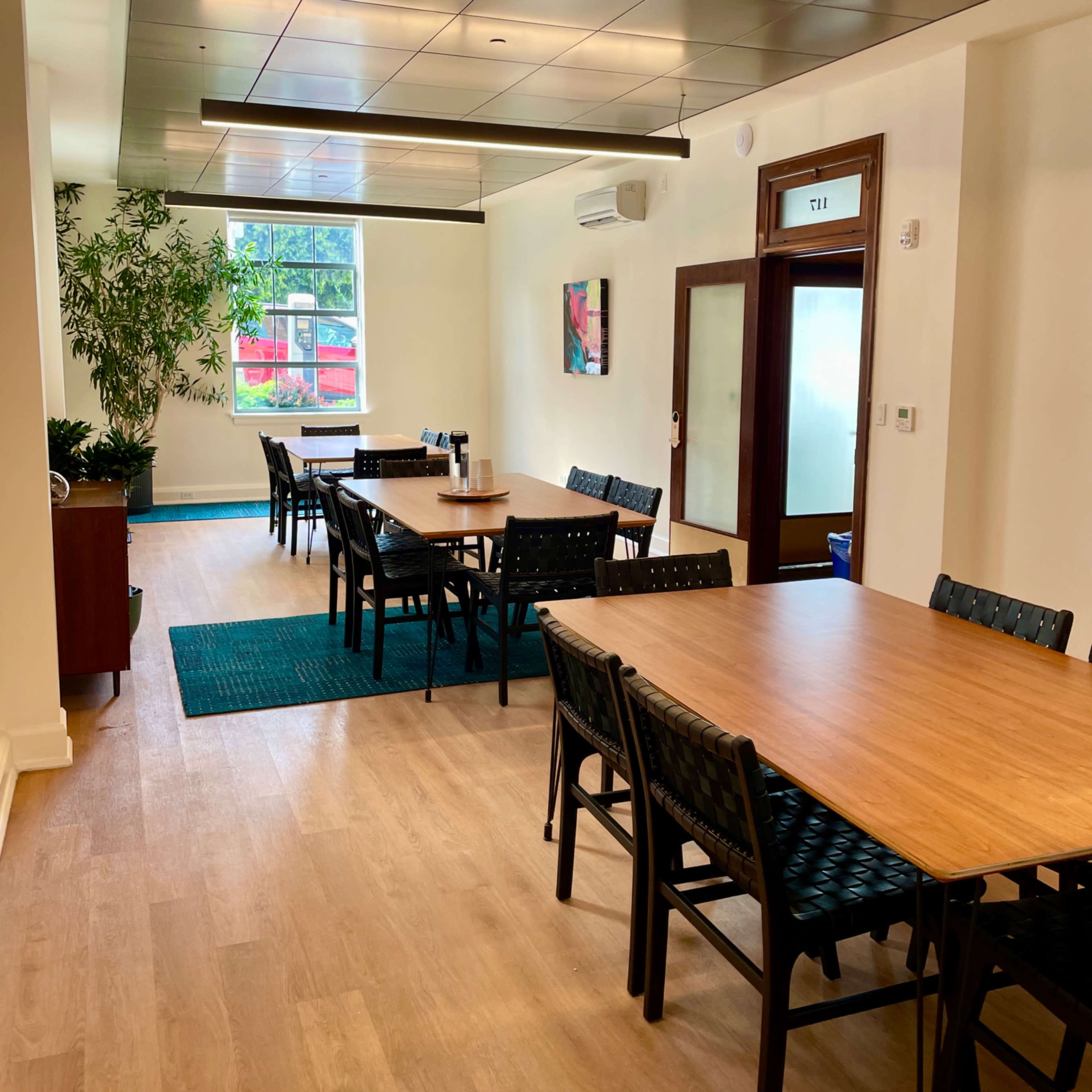 A well-arranged dining area with multiple wooden tables and chairs, illuminated by natural light from a window.