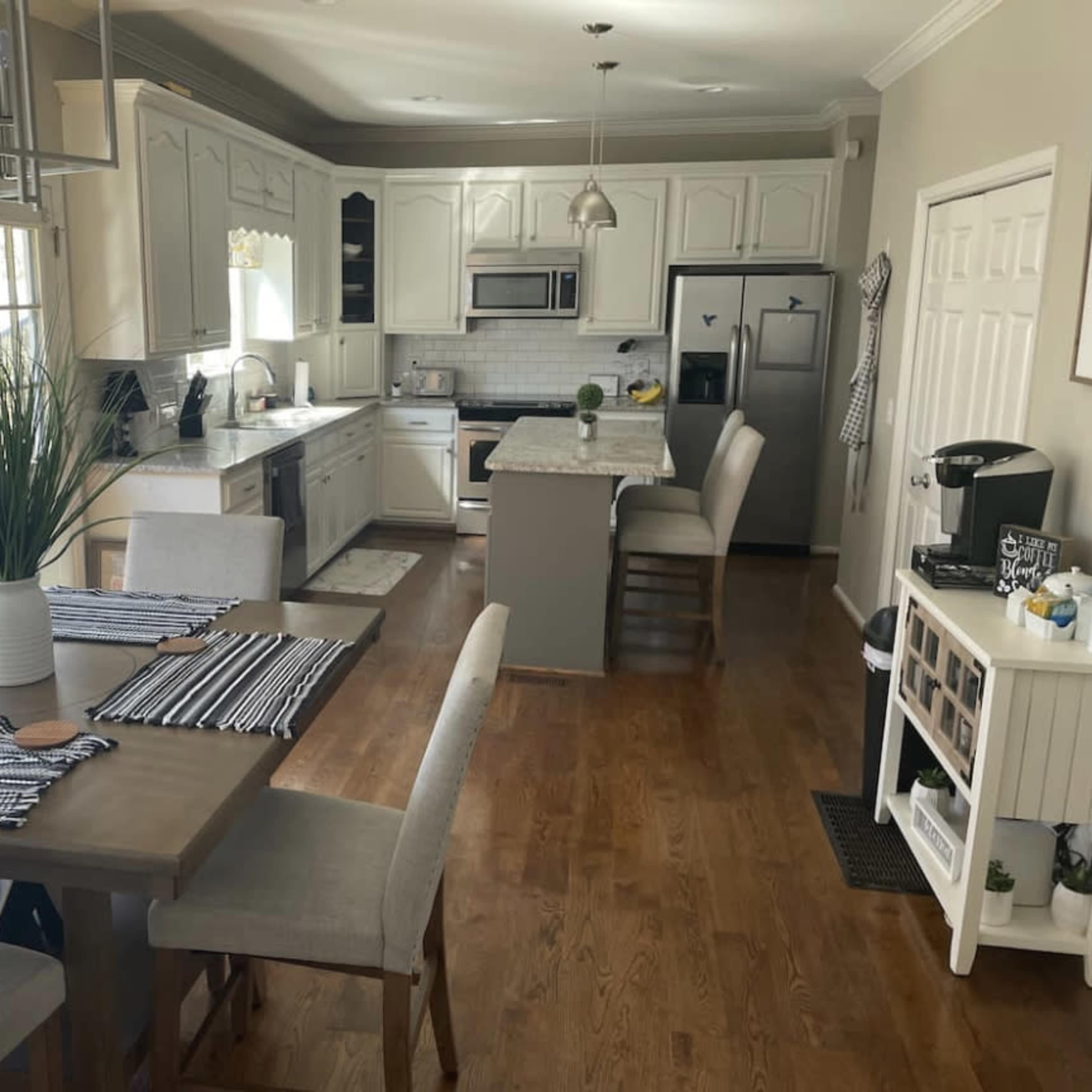 A modern kitchen and dining area with white cabinetry, a wooden table set for meals, and stainless steel appliances.