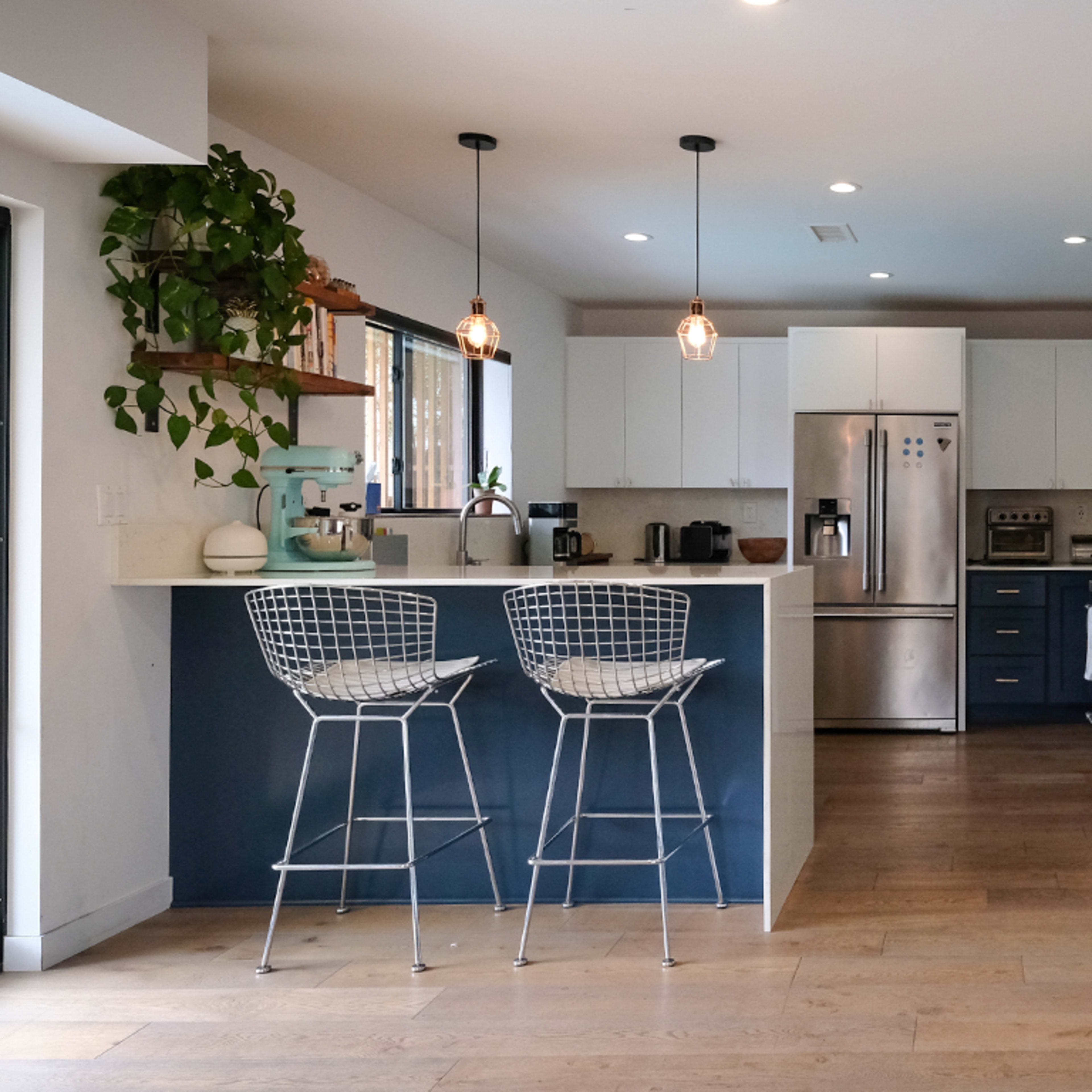 A modern kitchen with white cabinets, a stainless steel refrigerator, and a bar with two wire stools.
