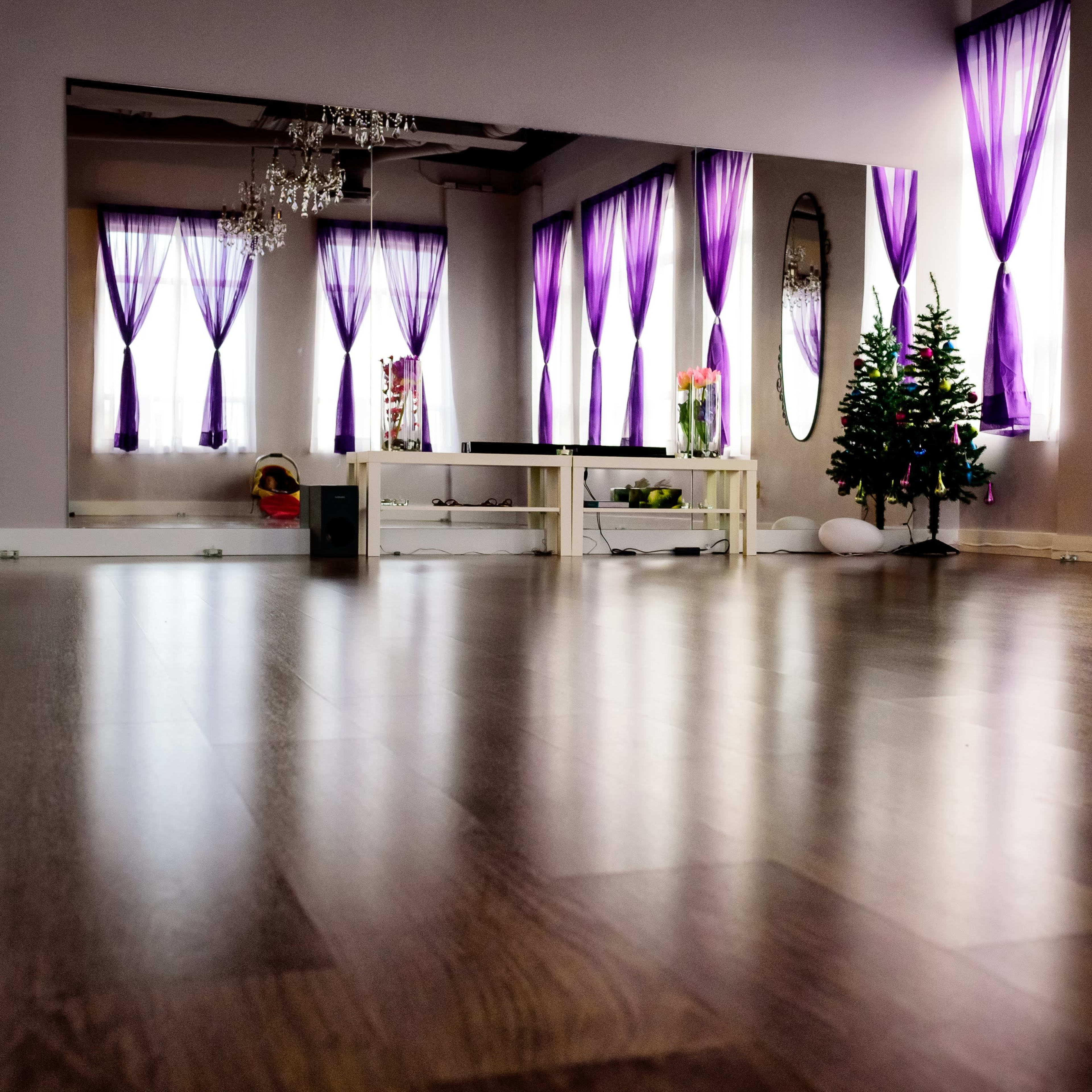 A spacious room with wooden flooring, large mirrors, and purple curtains, featuring a small Christmas tree in one corner.