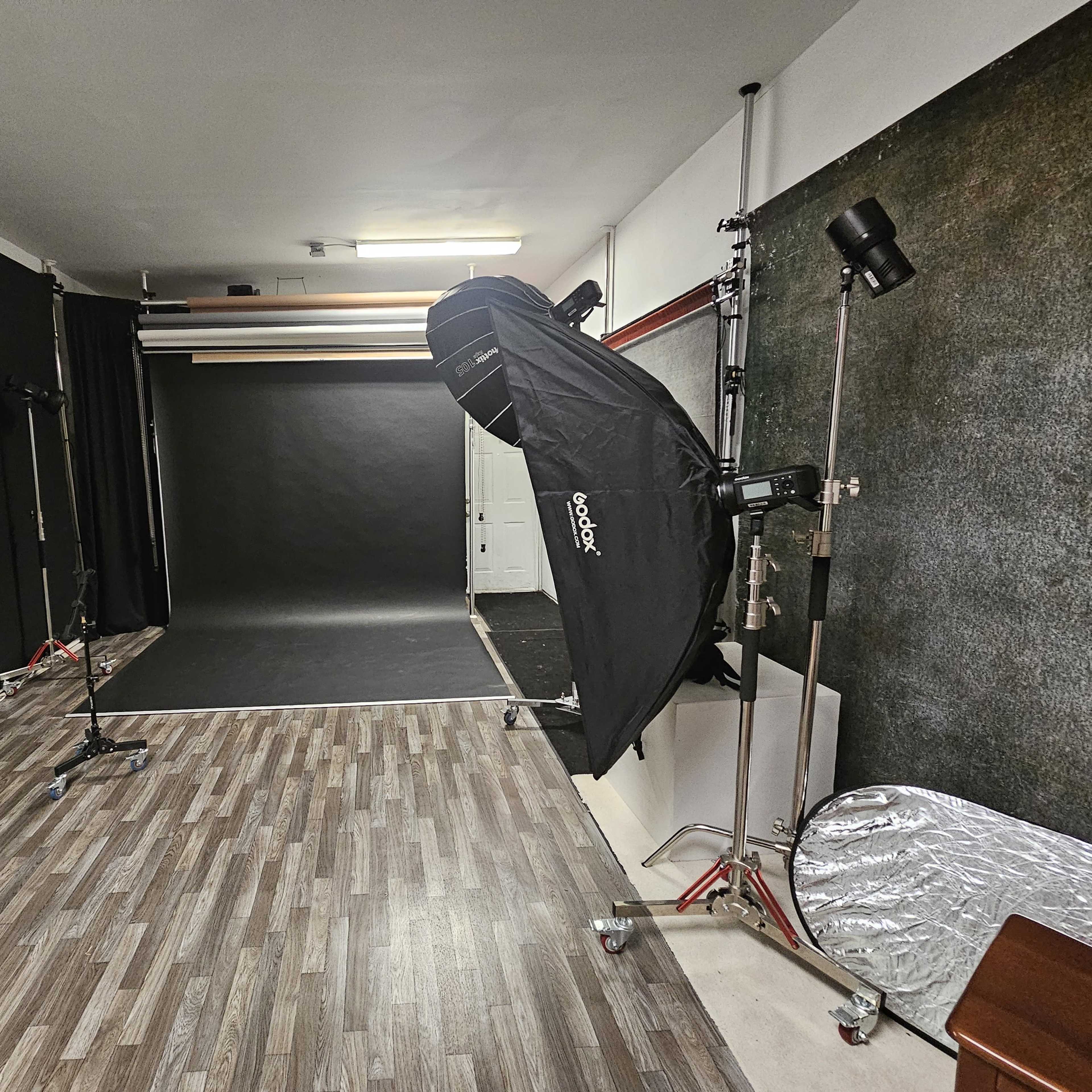 A photography studio equipped with lighting setups, a dark backdrop, and wooden flooring.