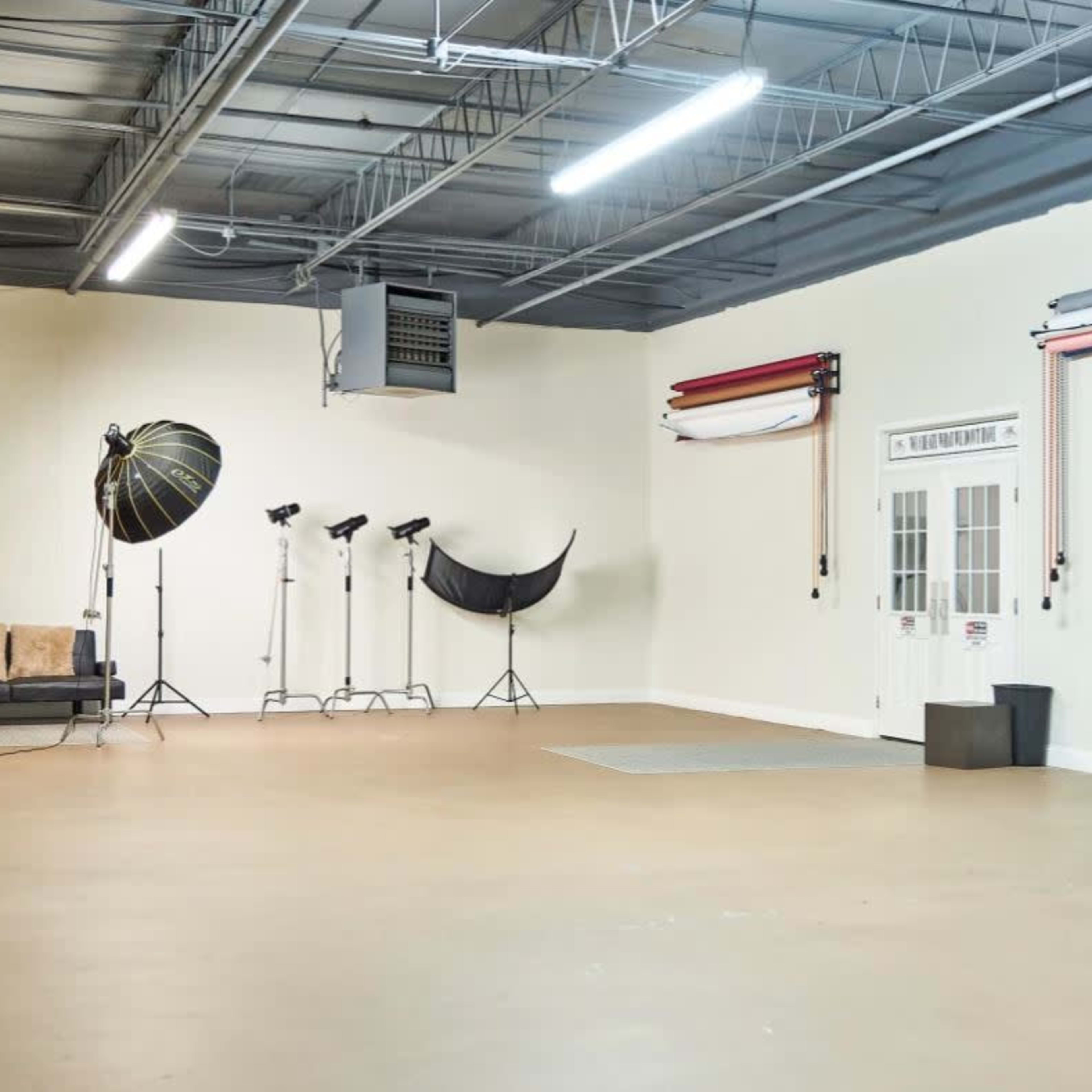 An empty photography studio with various lighting equipment, a couch, and a door leading outside.