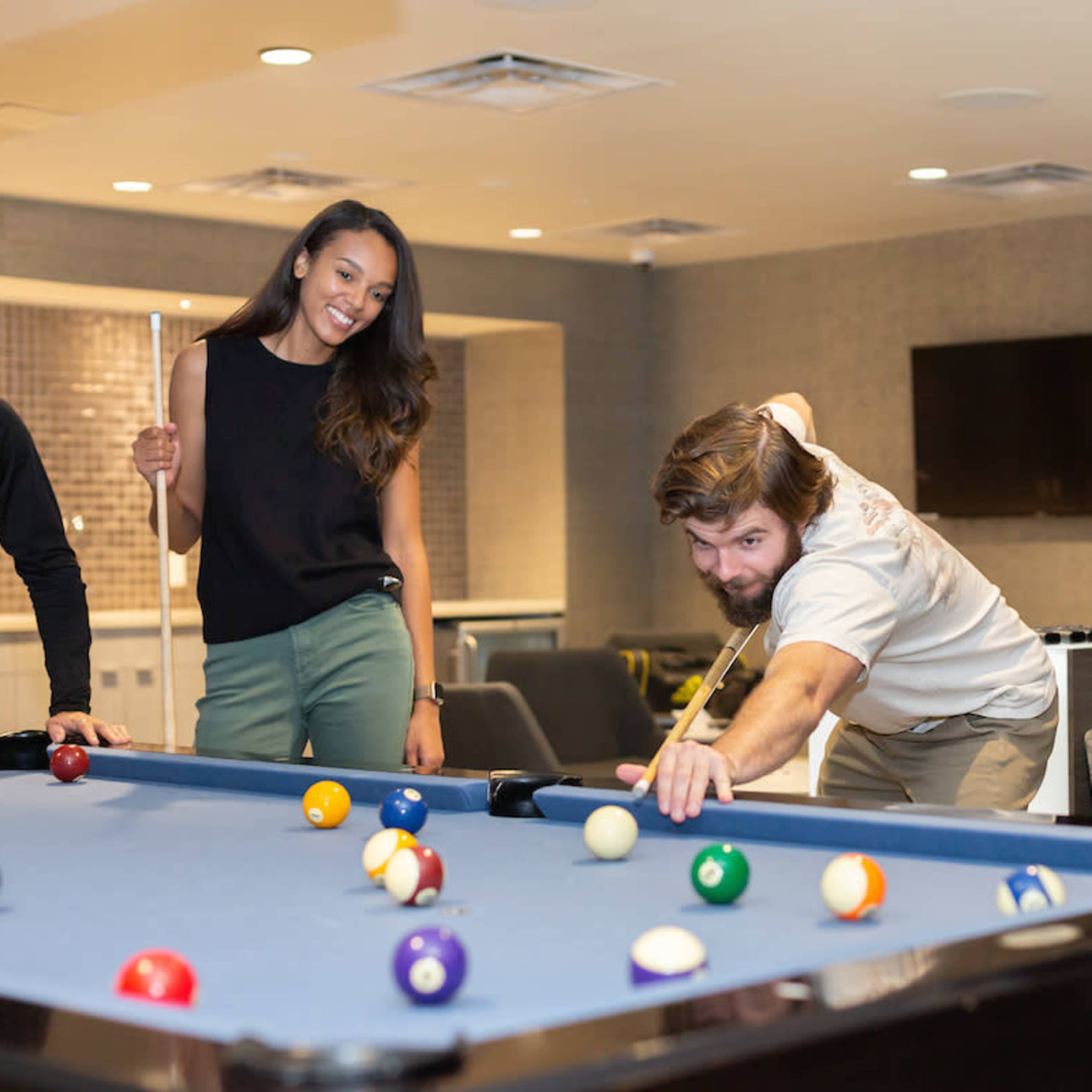 A group of four people play pool in a recreational room with a blue billiard table.