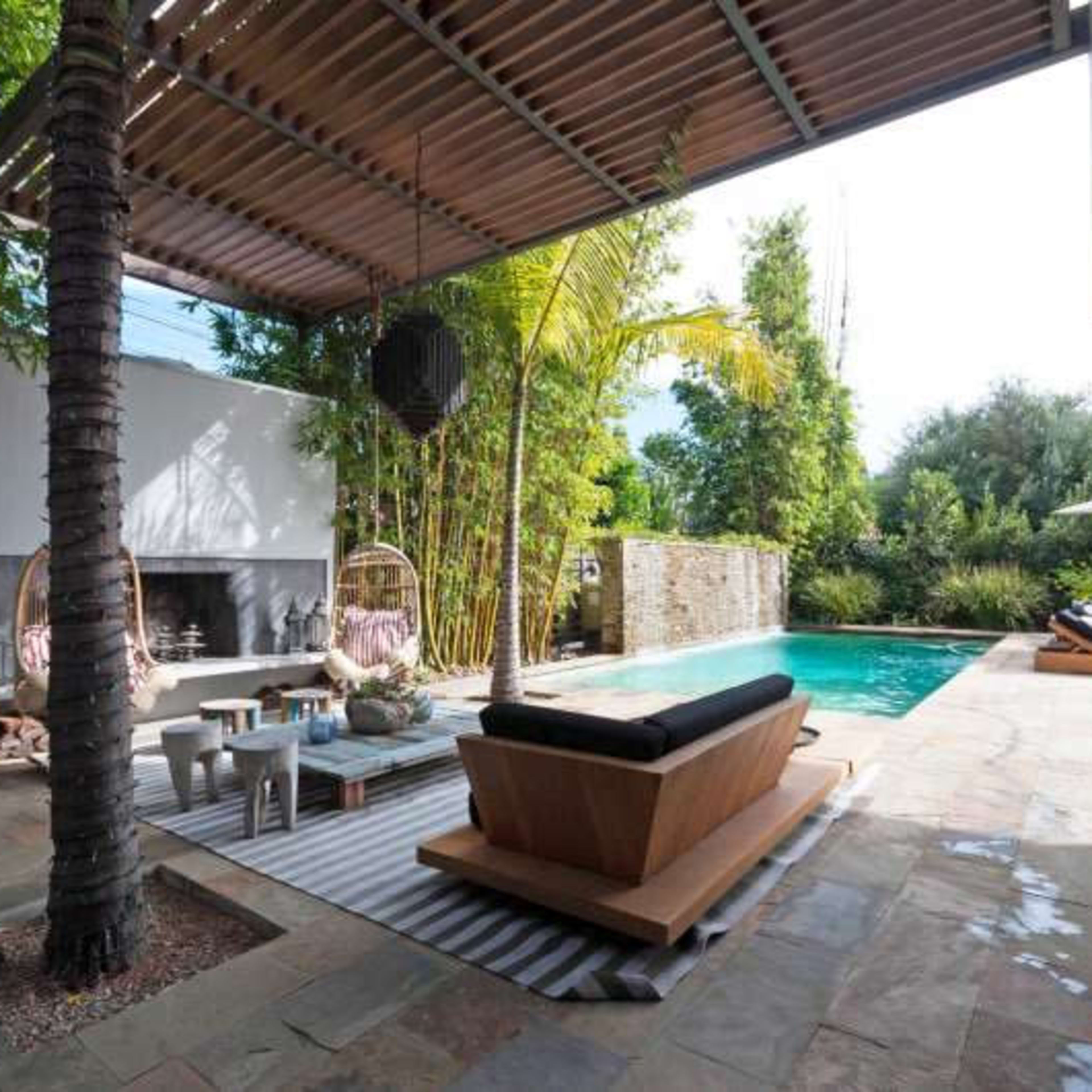 A spacious outdoor area with a swimming pool, modern seating, and tropical plants, all beneath a shaded patio.