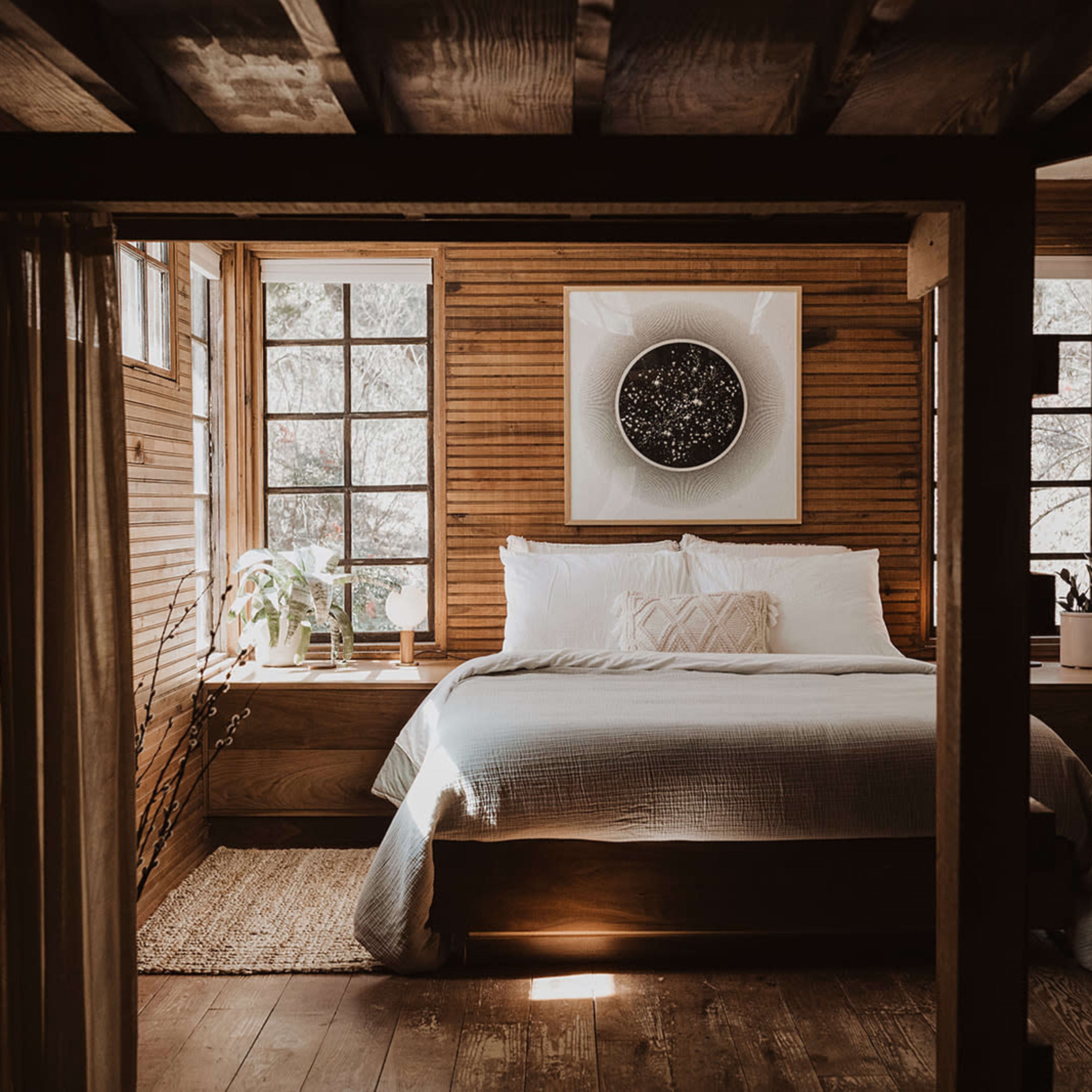 A cozy bedroom with wooden walls, a large bed in the center, and large windows allowing natural light to enter.