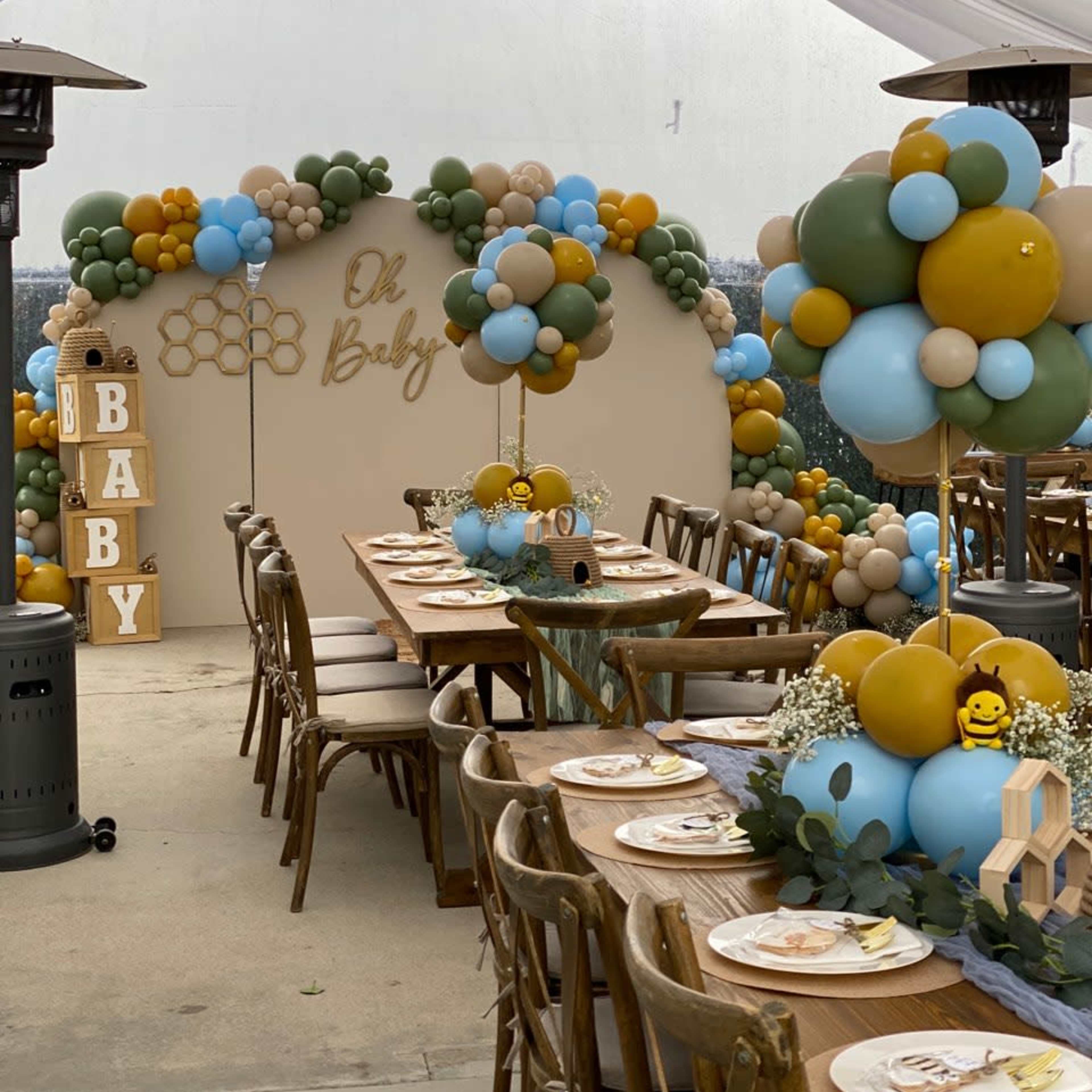 A beautifully decorated party space with a "Oh Baby" theme, featuring balloon arrangements in blue, beige, and green, and a long wooden table set for guests.
