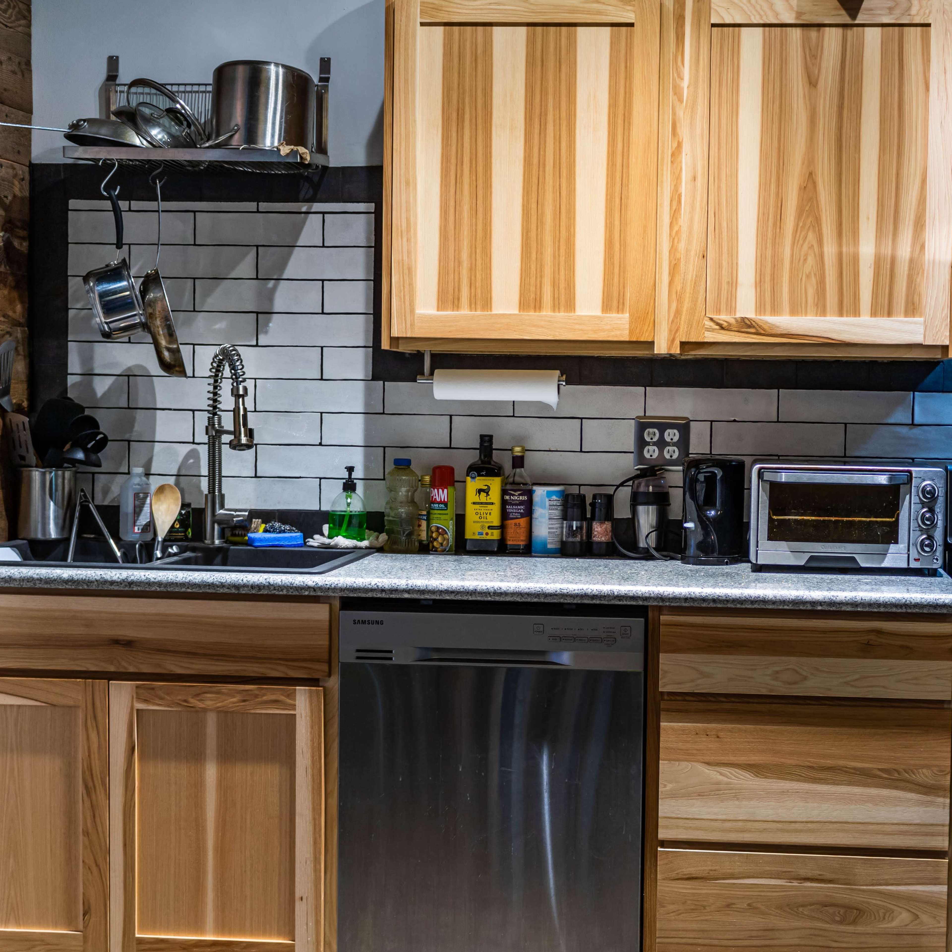 A modern kitchen with wooden cabinets, a stainless steel dishwasher, a gas range, and various kitchen appliances on a countertop.