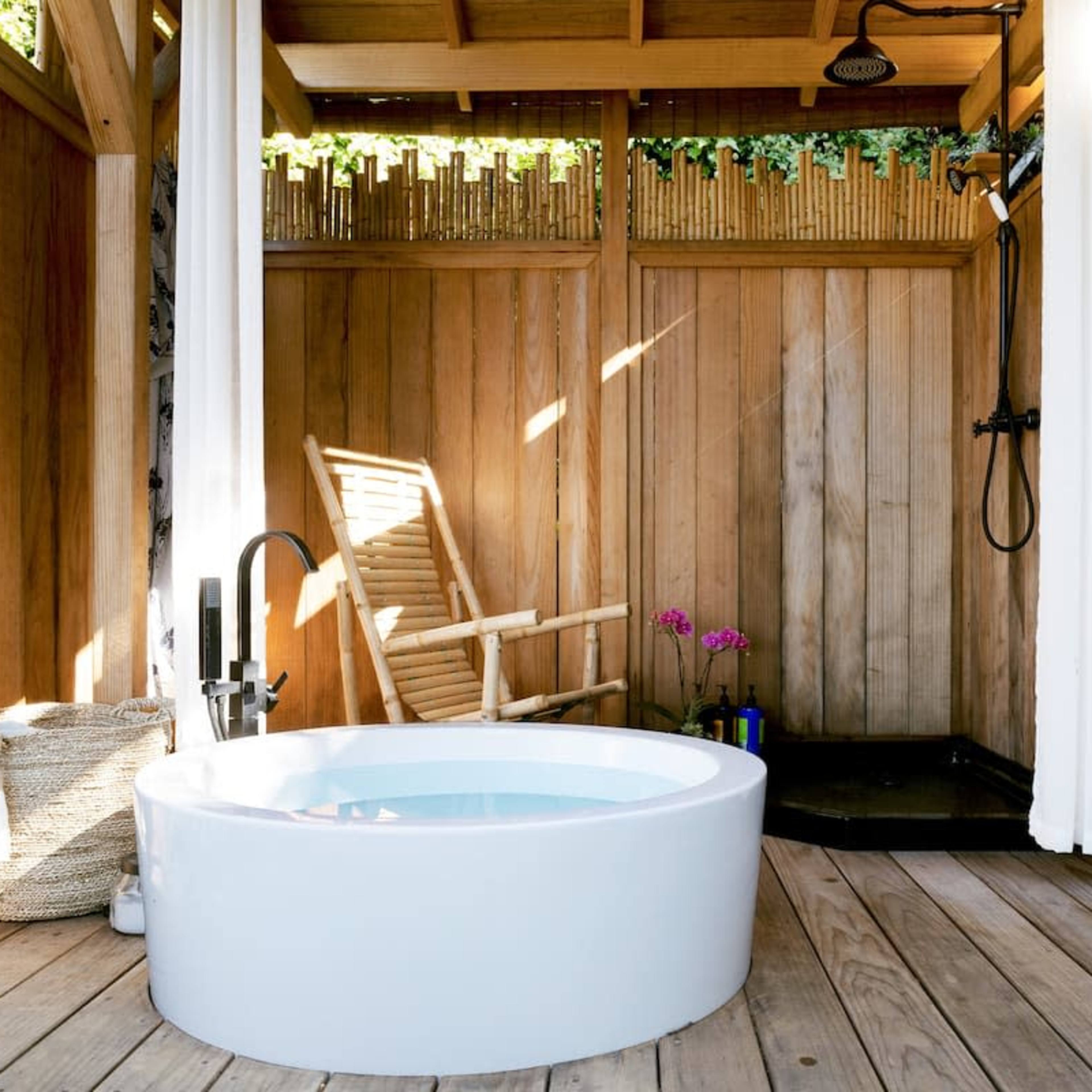 A modern bathroom with a circular white bathtub, wooden walls, a shower area, and a chair beside a potted plant.