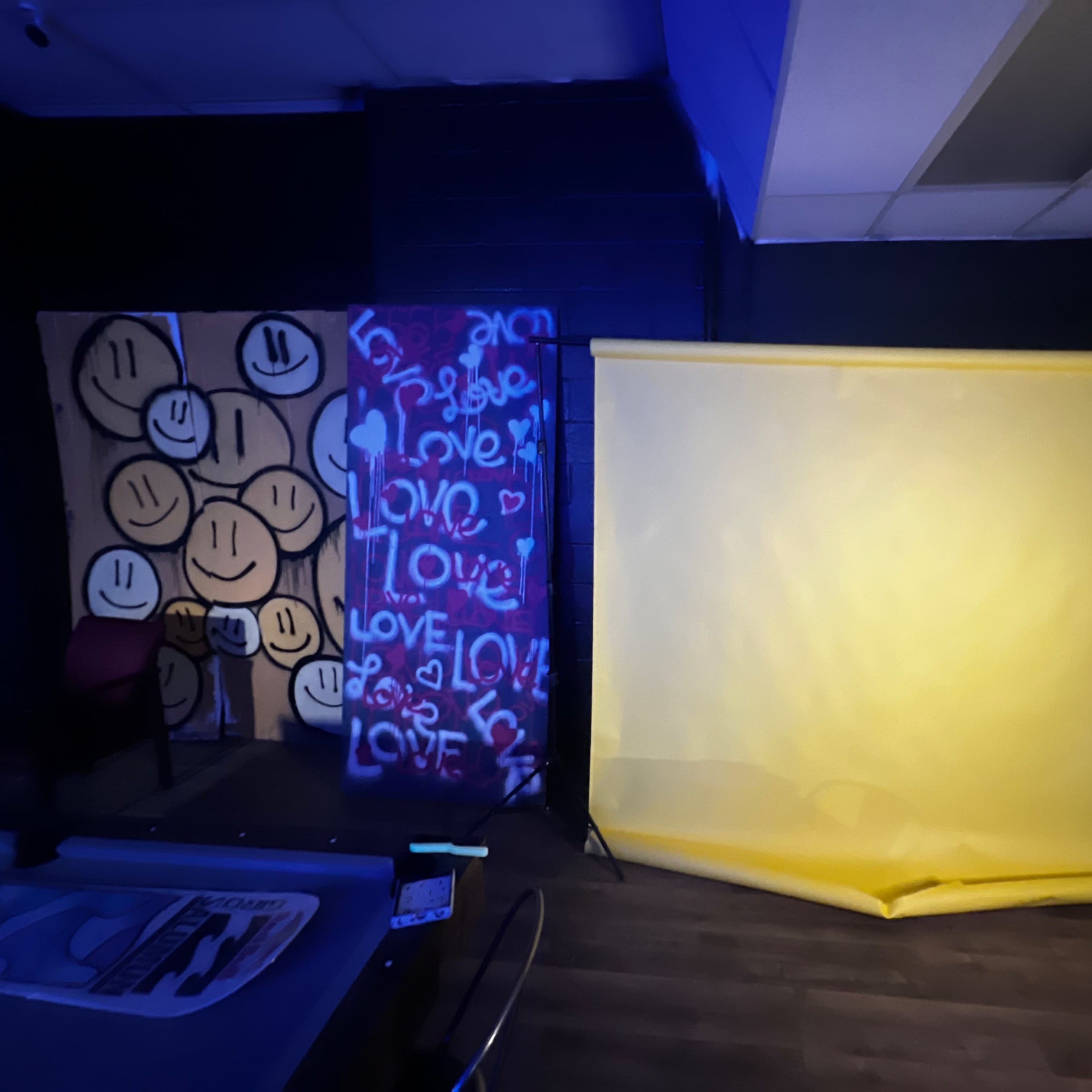 The scene shows a room with a yellow backdrop and a wall featuring various smiley faces and colorful graffiti that includes the word "love."