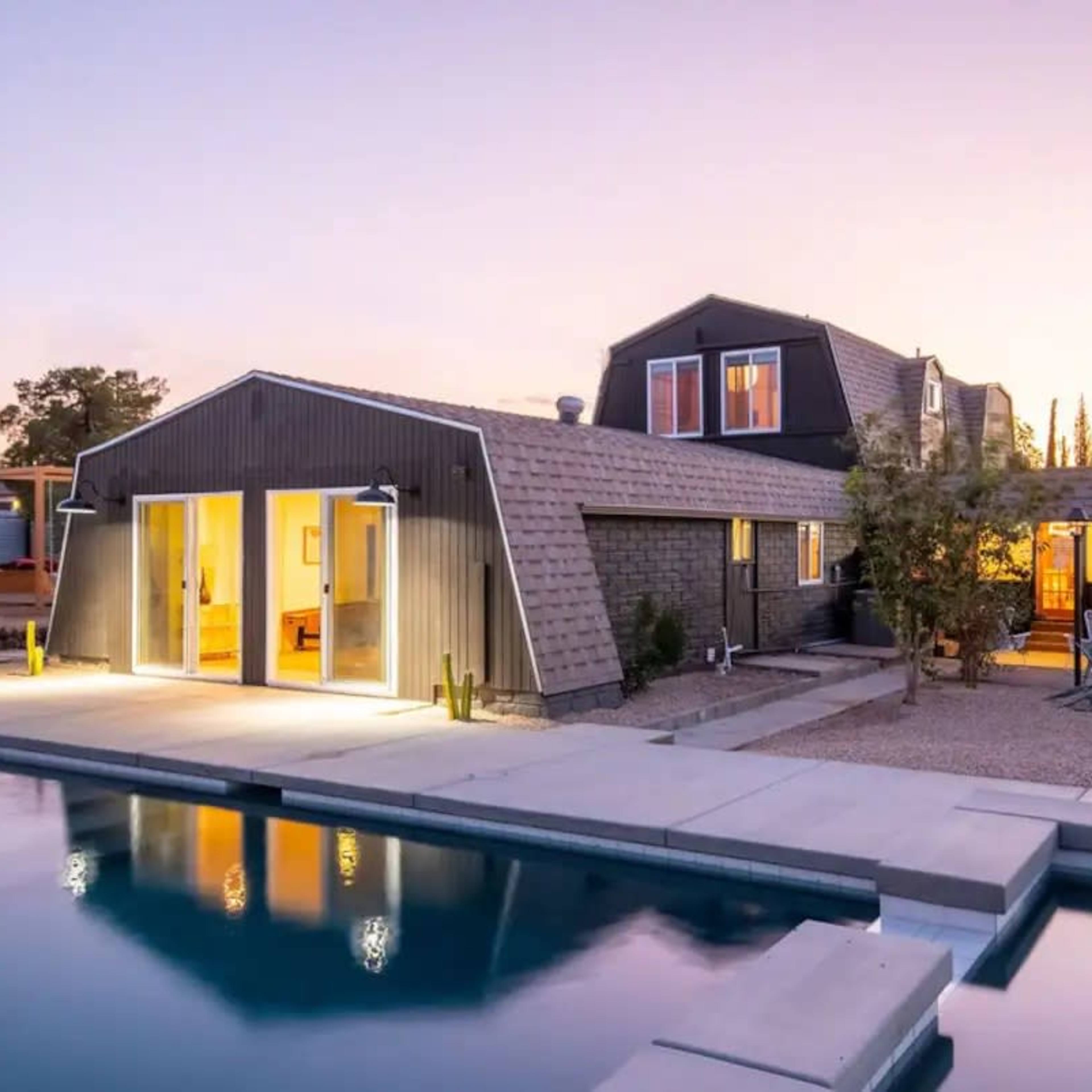 A modern house with a sloped roof is situated near a pool, reflecting the twilight sky.