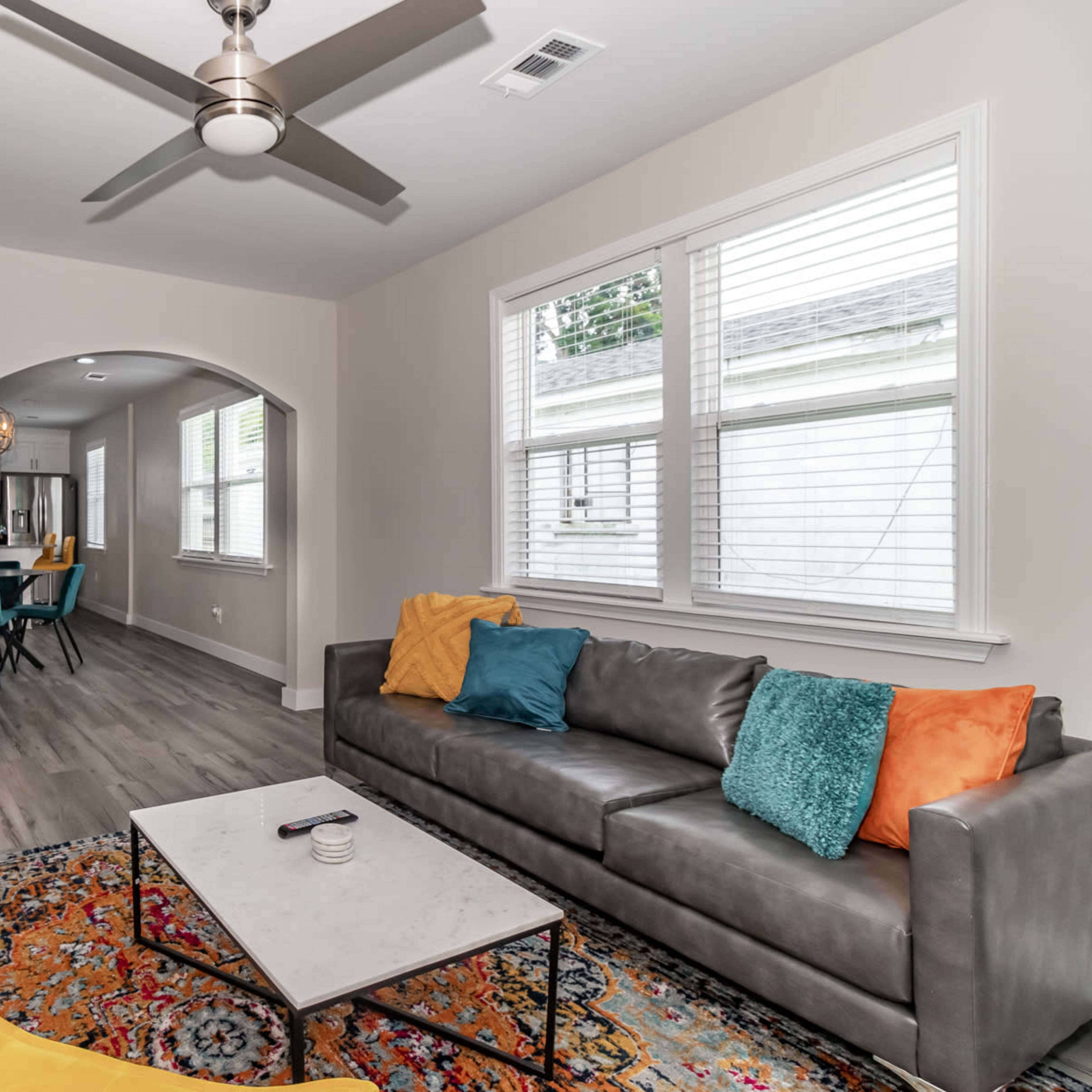 The living room features a gray sofa with colorful pillows, a coffee table on a patterned rug, and a television mounted above a white brick fireplace.