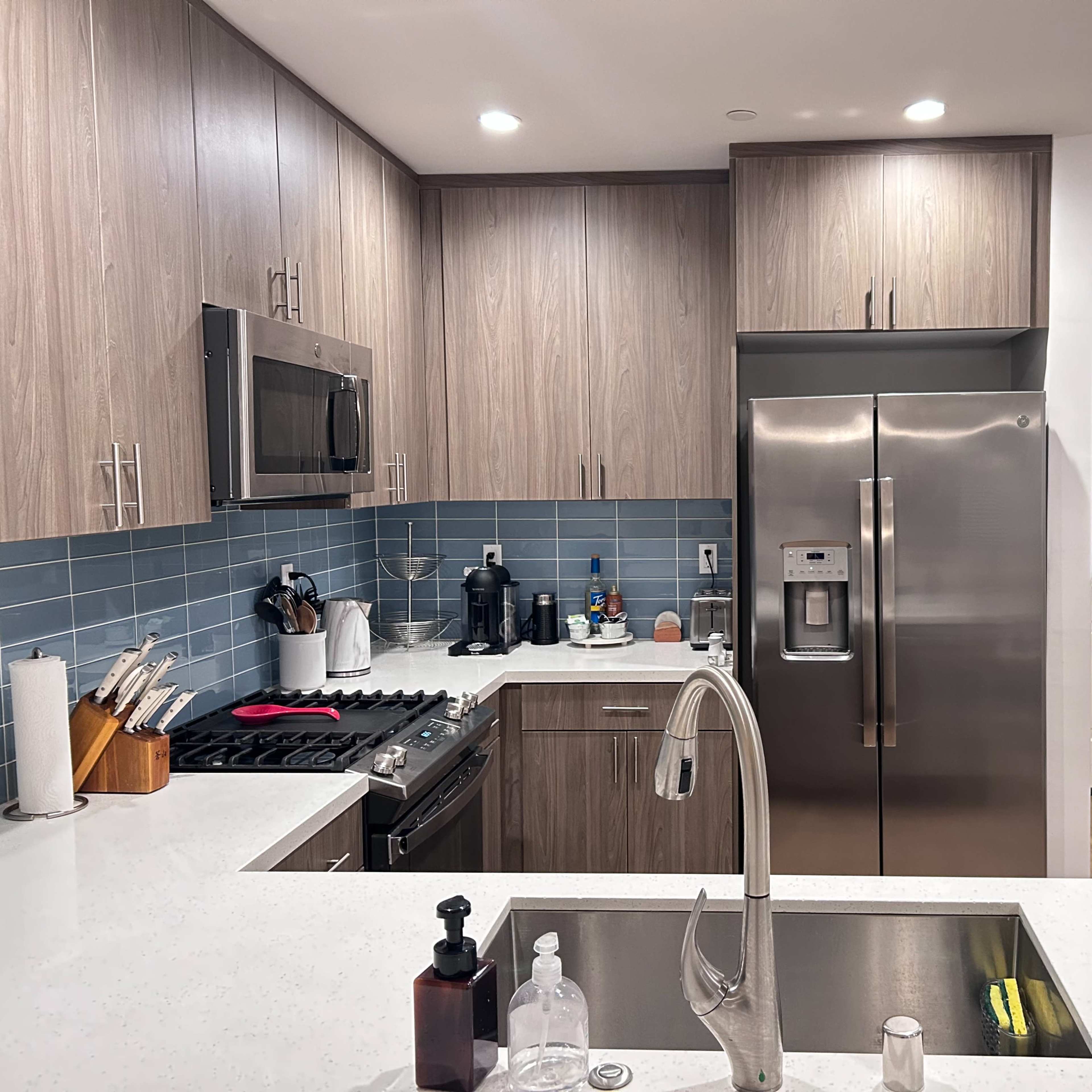 The kitchen features modern cabinets, stainless steel appliances, and a blue tile backsplash, with a view of an entrance door.