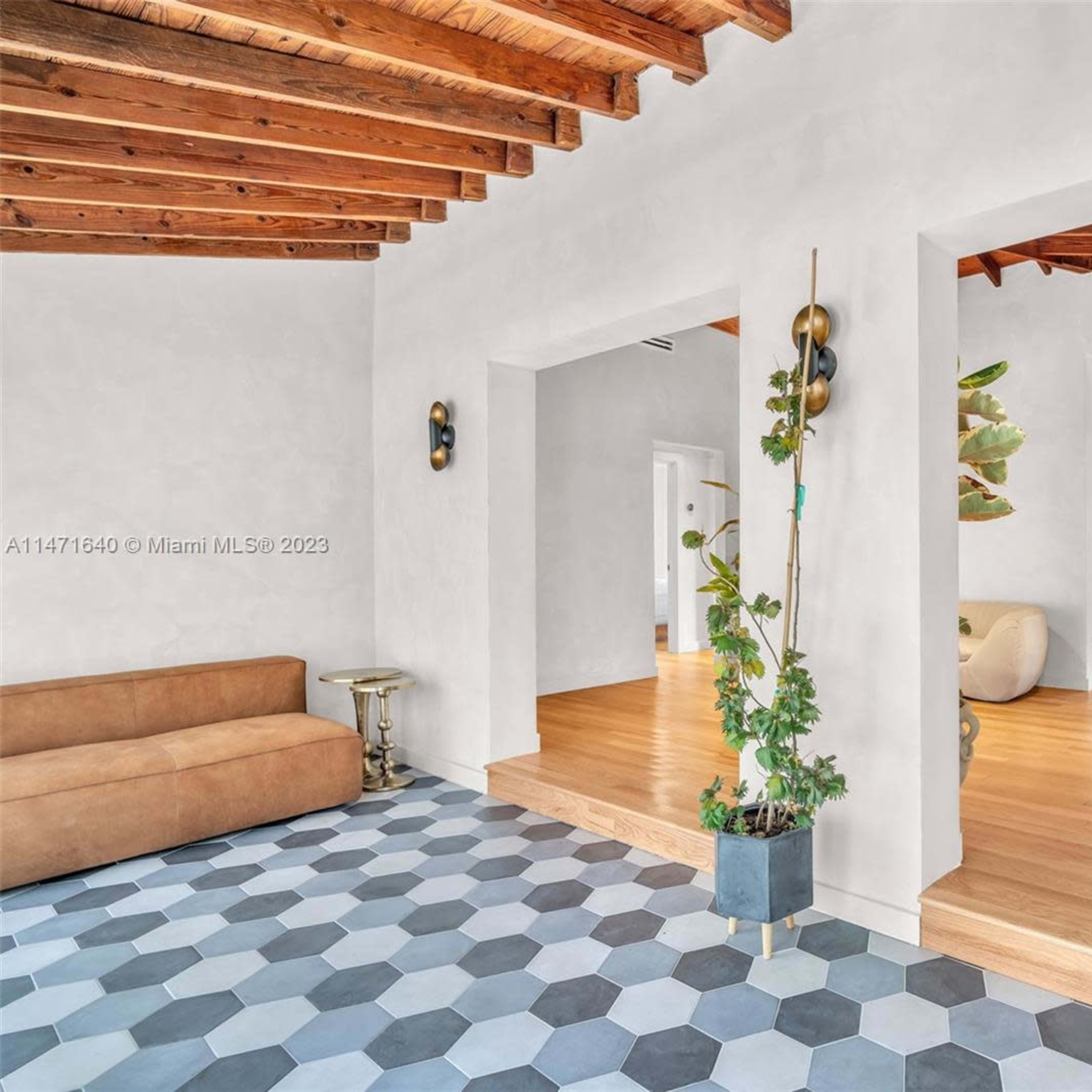 A living space features exposed wooden beams, a combination of tile and hardwood flooring, and an open layout connecting to a dining area.