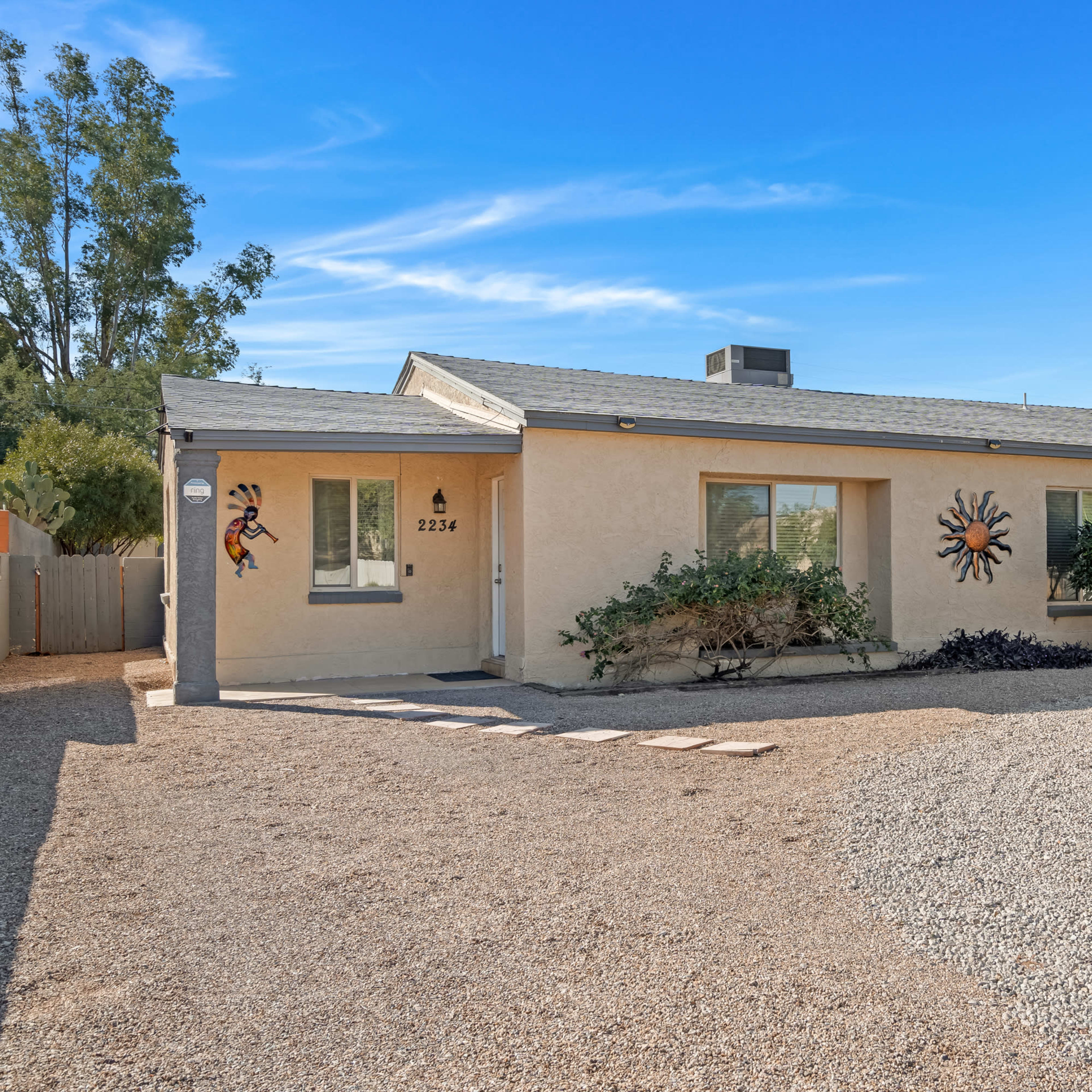 A single-story house with decorative wall art, surrounded by gravel landscaping and sparse vegetation.