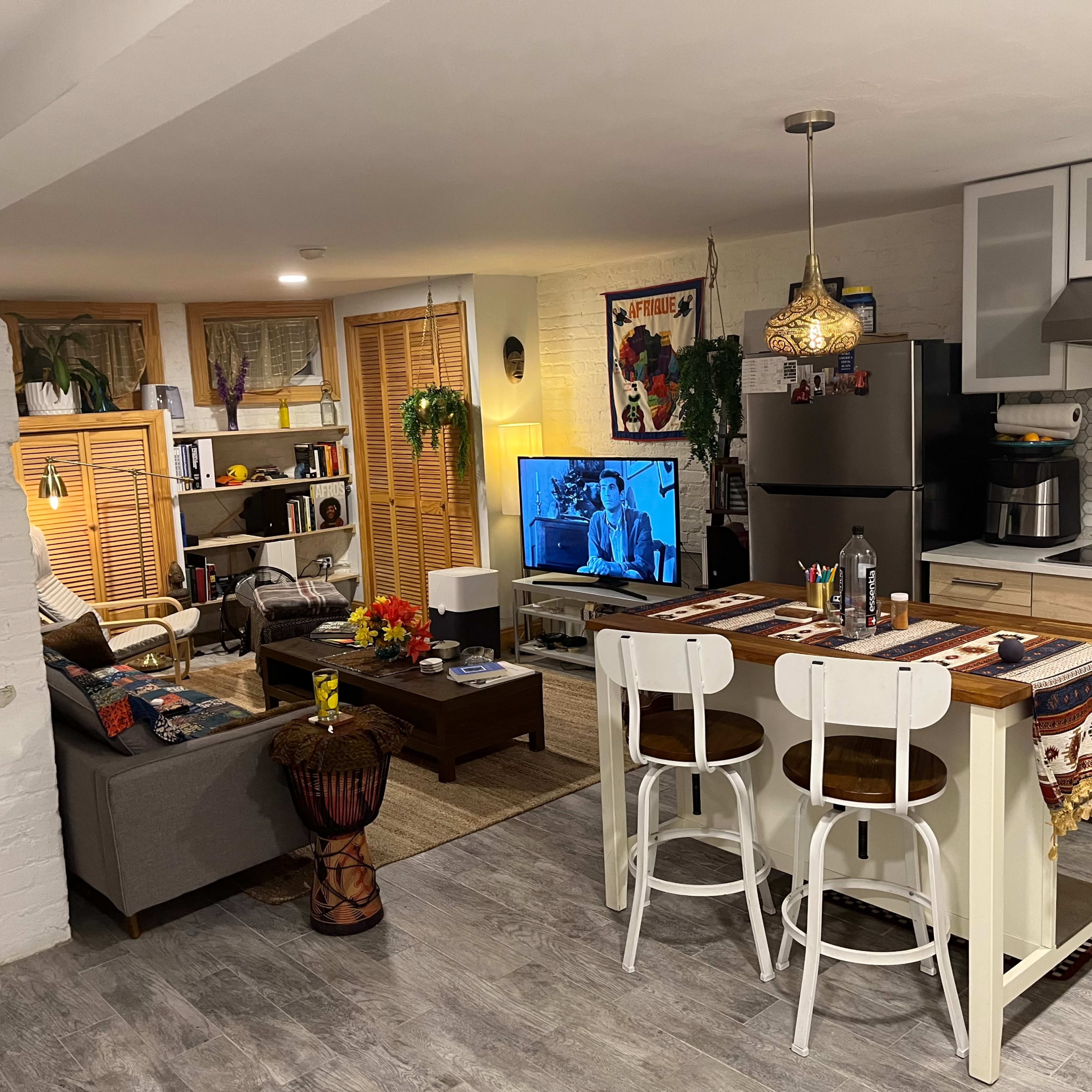 A modern kitchen and living area with a dining table, a sofa, a television, and decorative plants.