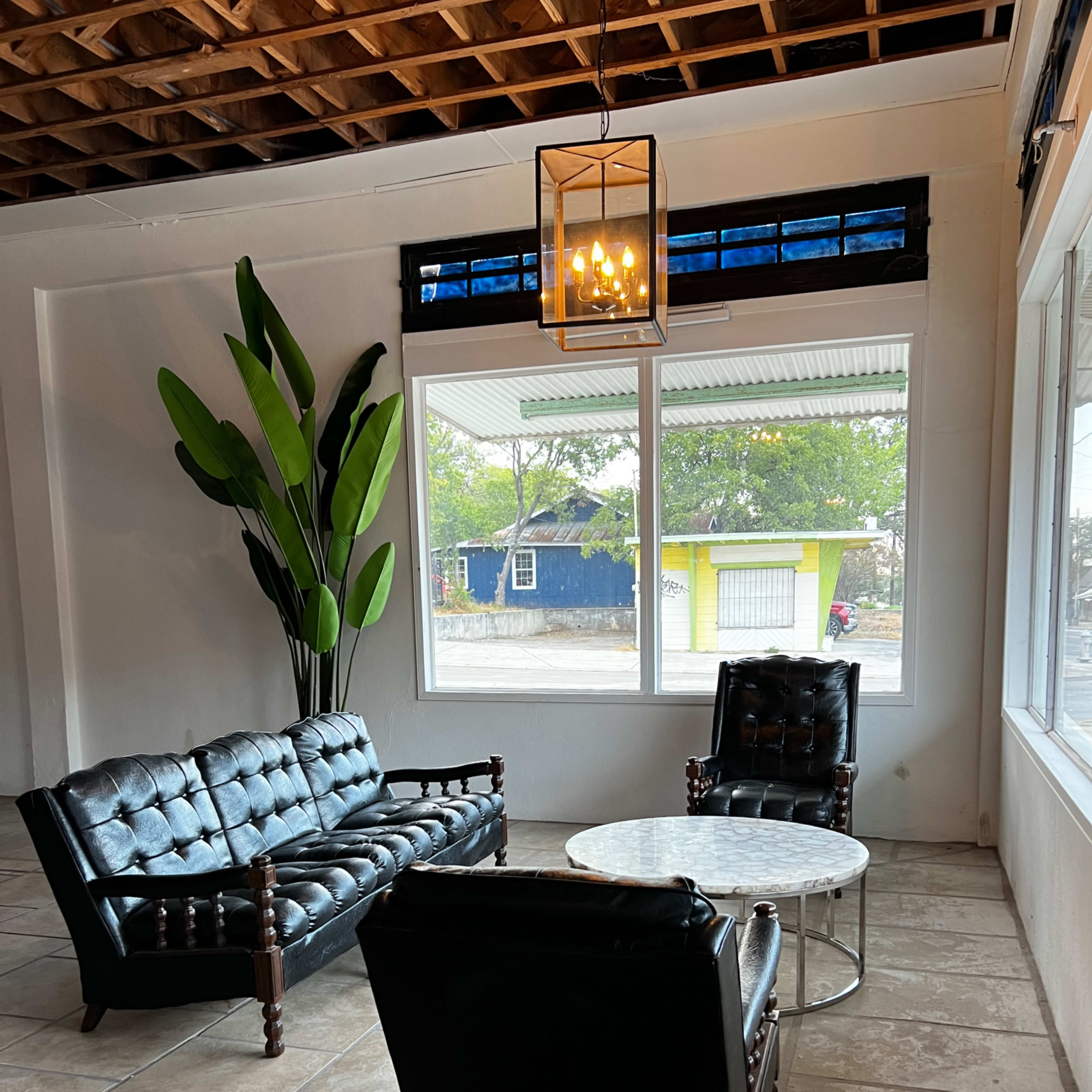 A seating area with a tufted black leather sofa, a pair of matching armchairs, a round marble coffee table, and a large potted plant next to a window.