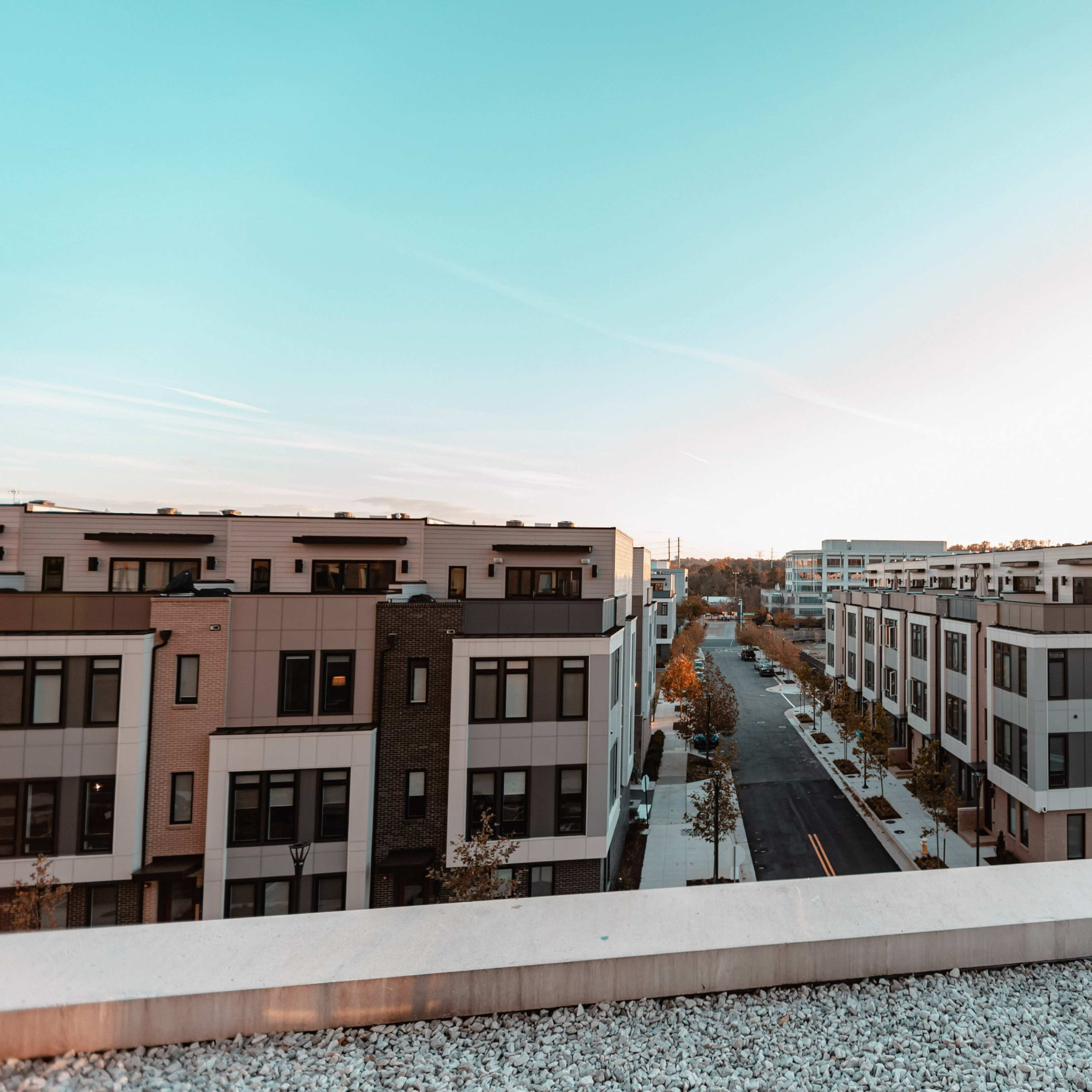 A modern residential neighborhood with multi-story buildings lining a quiet street under a clear sky at sunset.