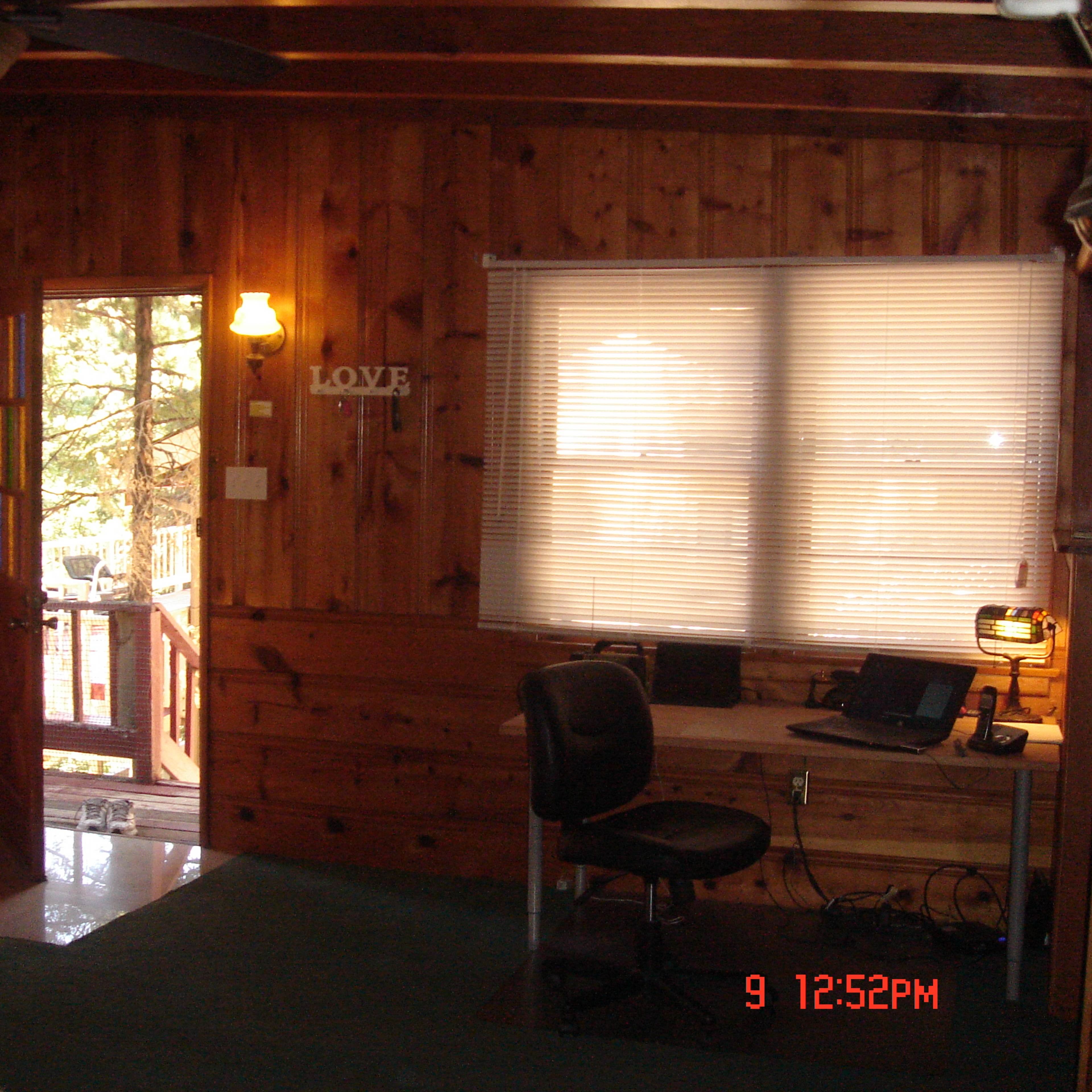 A wooden interior room with a desk and computer, a door leading outside, and a decorative "LOVE" sign on the wall.