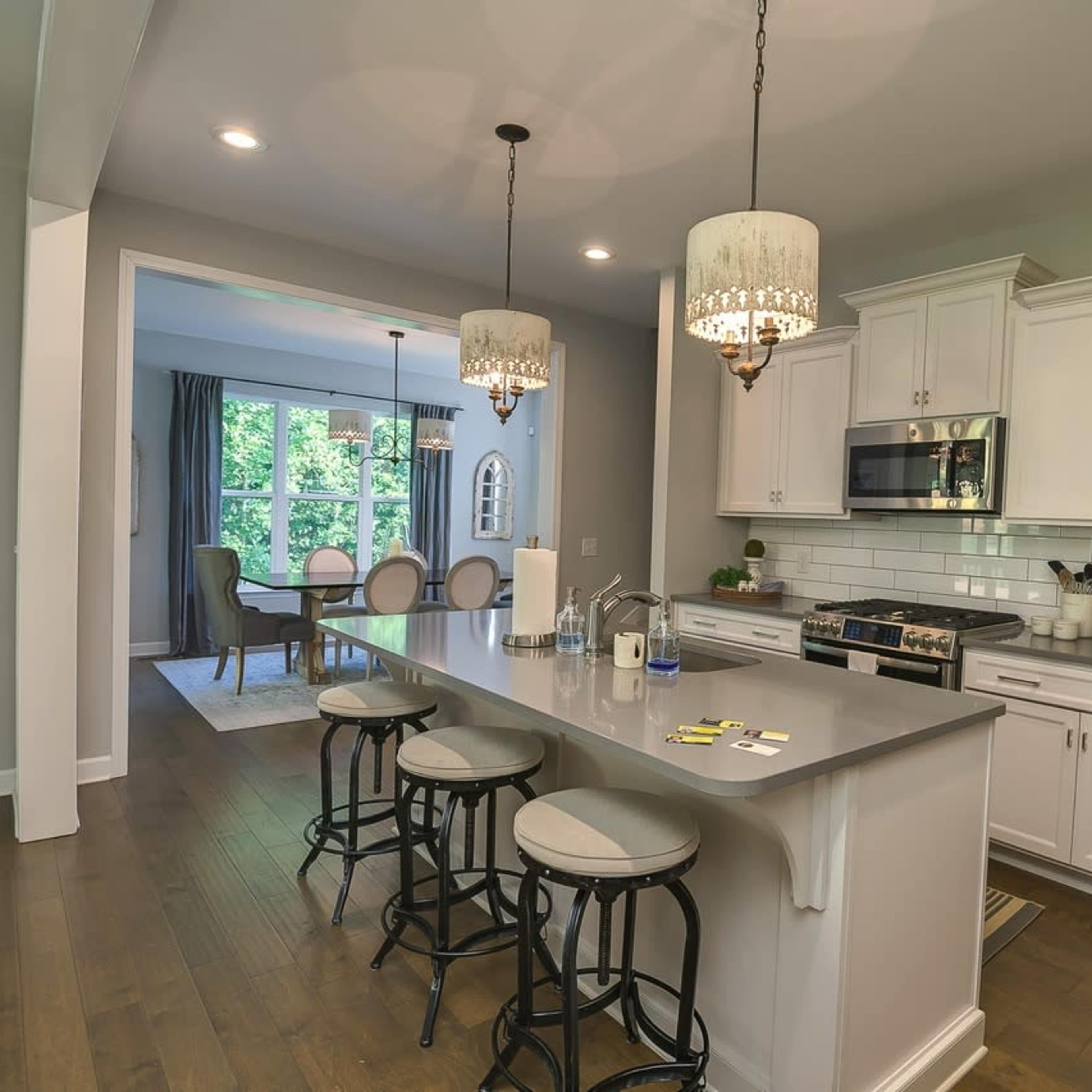 A modern kitchen with white cabinets, stainless steel appliances, and a large island featuring three bar stools, connected to a dining area with a table and chairs in the background.