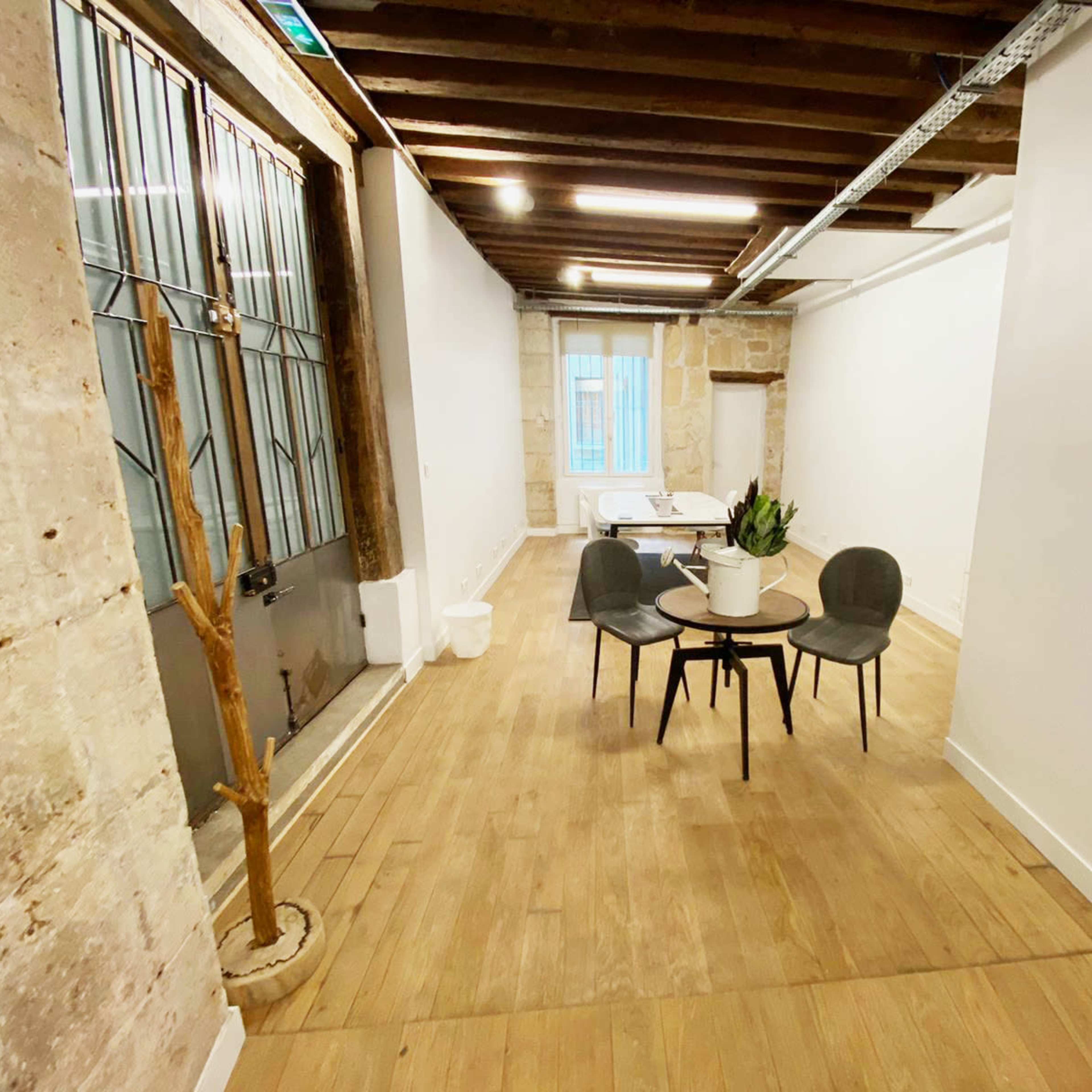 A sparsely furnished interior space featuring a small table with four chairs, wooden flooring, and a large window at the far end.