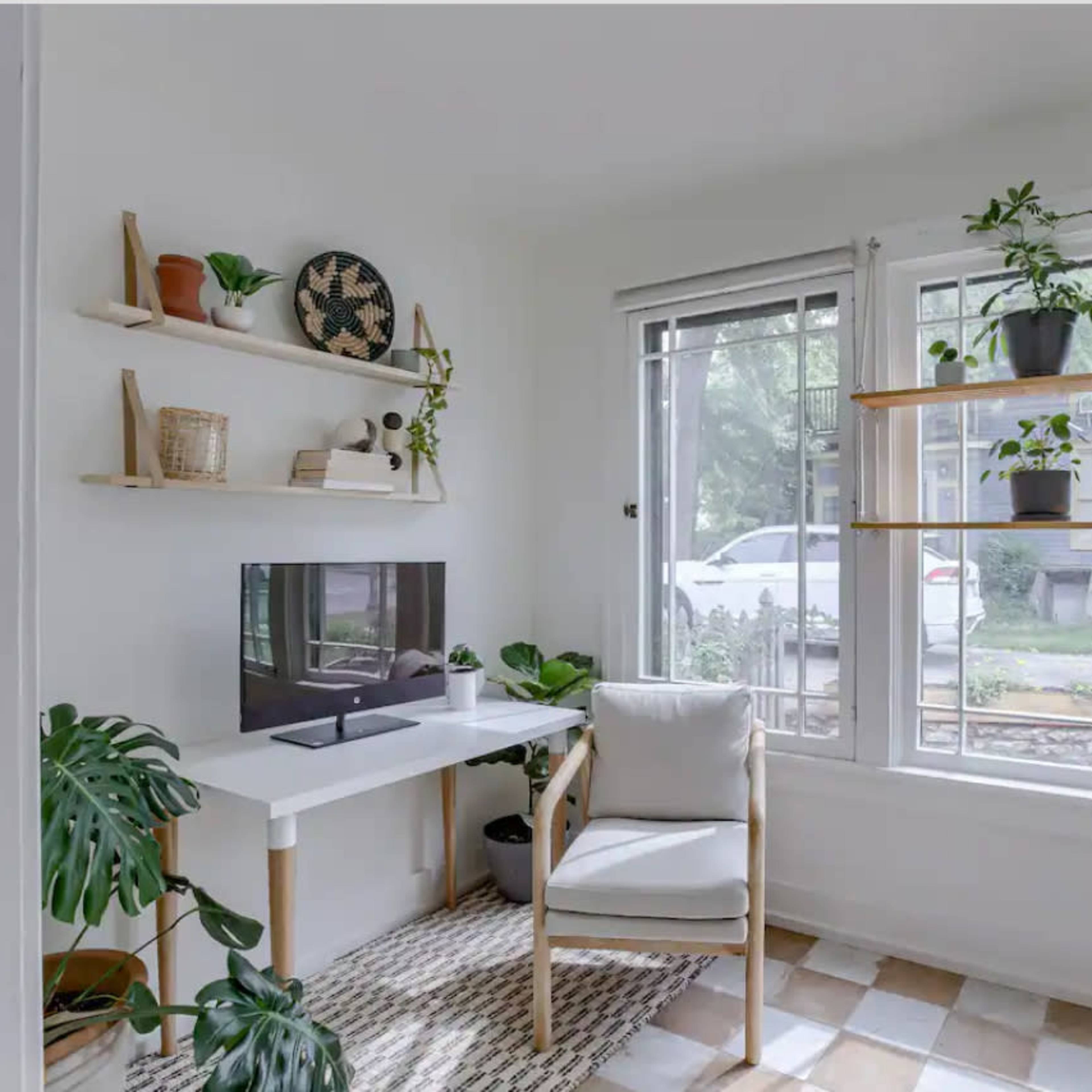 A cozy office space features a white desk with a television, a comfortable chair, and several shelves adorned with decorative items and plants.