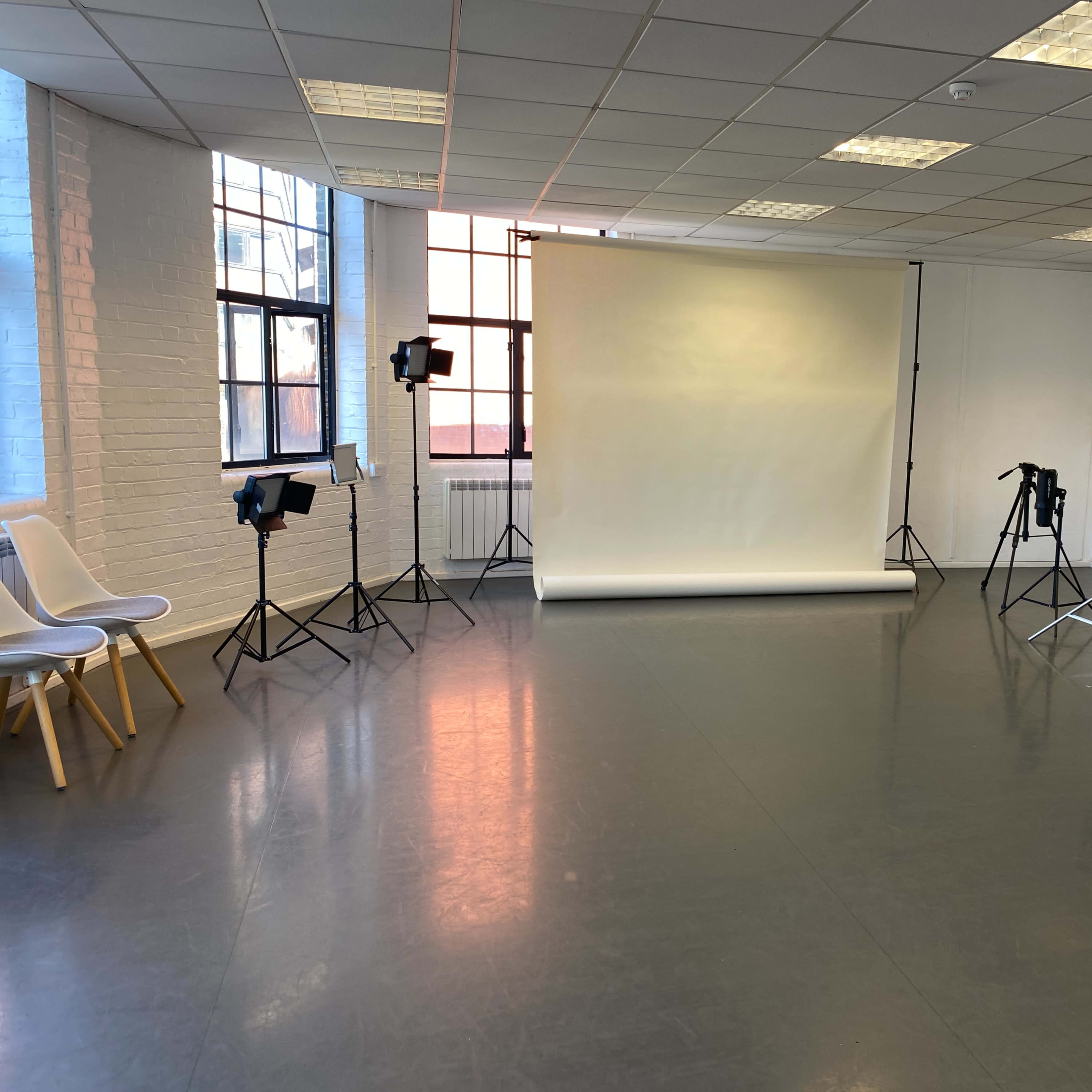 A photography studio with a seamless backdrop, lighting equipment set up on stands, and minimalist seating in a spacious room.