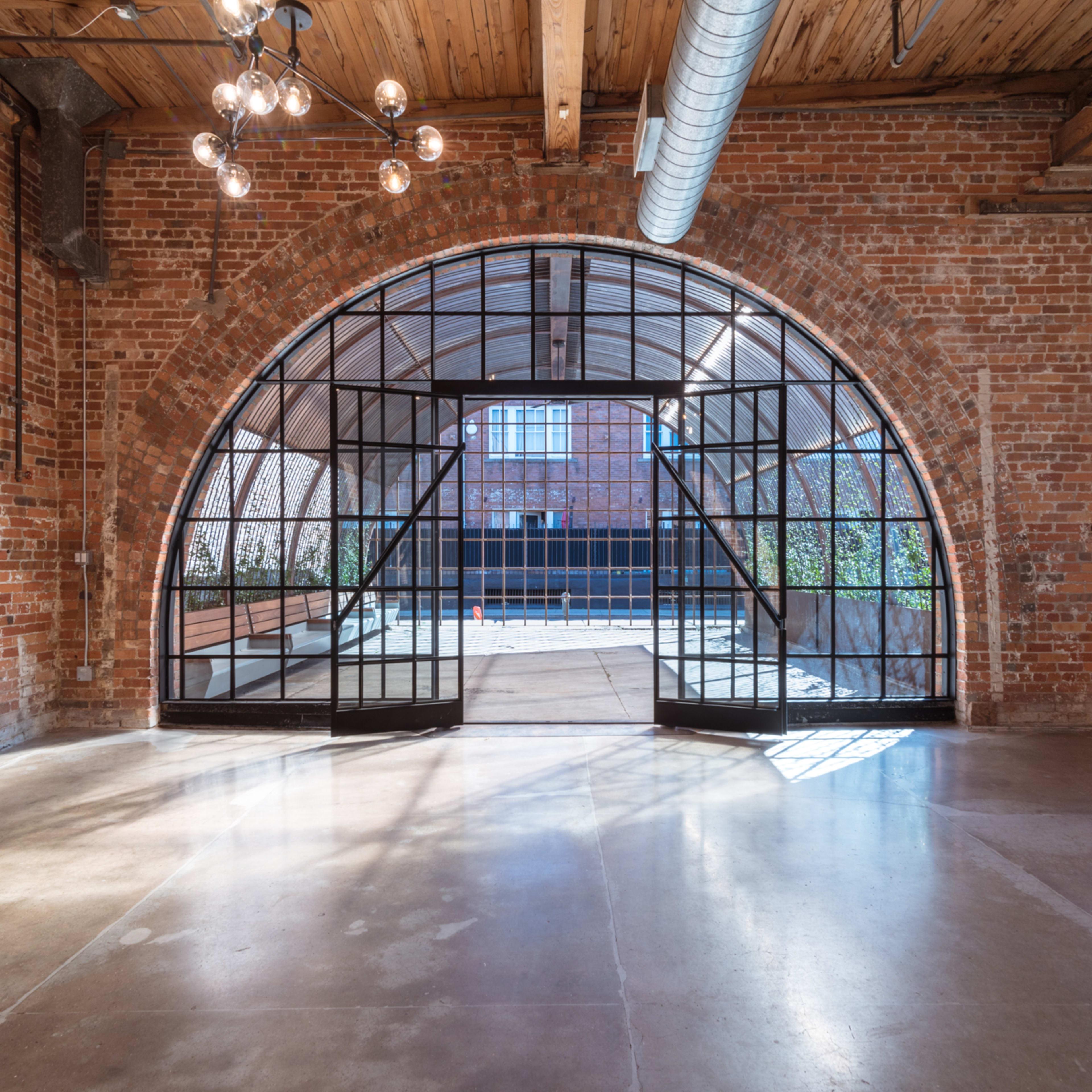An expansive, brick-walled interior featuring a large arched glass door that leads to an outdoor area.