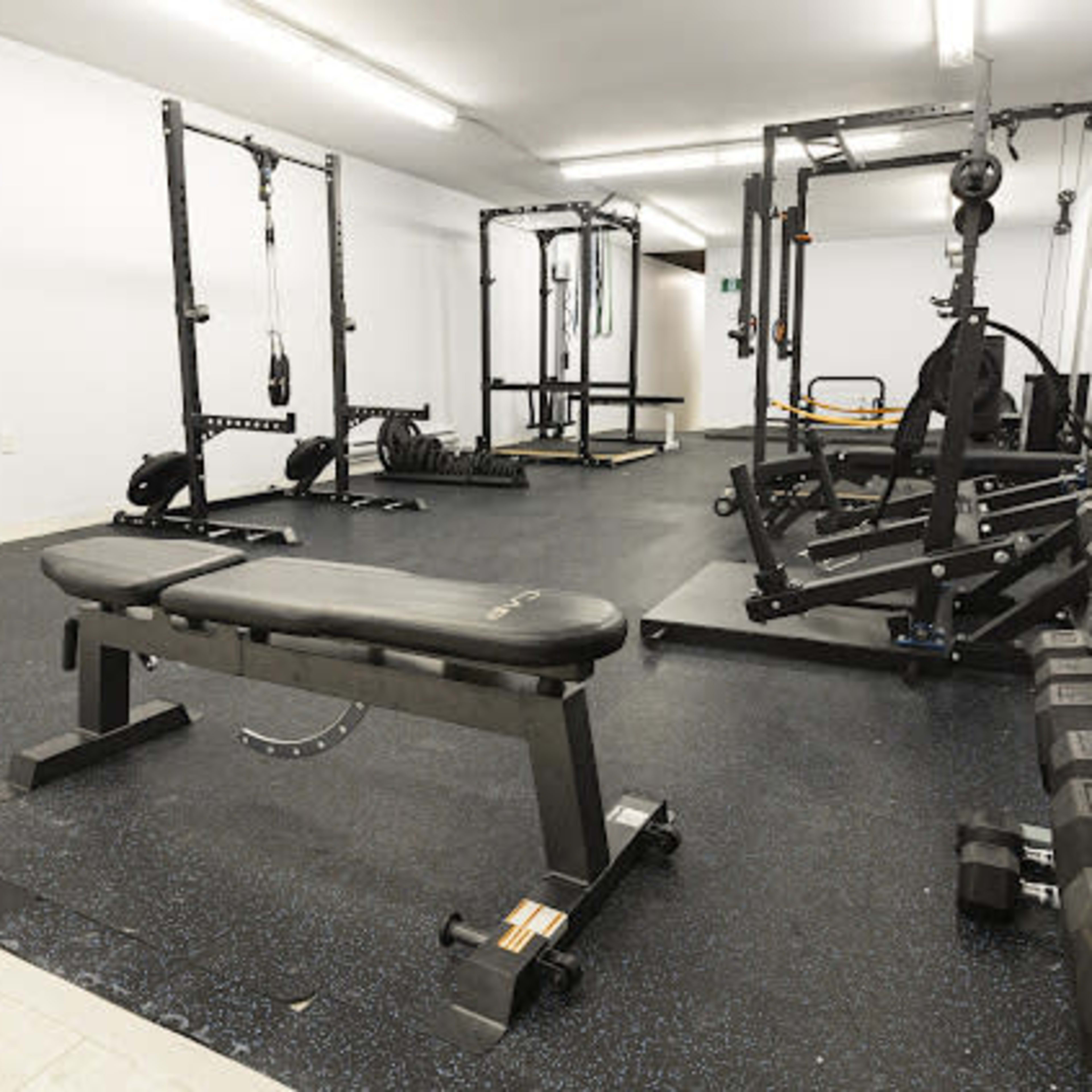 A spacious fitness room equipped with various weightlifting machines, dumbbells, and an adjustable bench.
