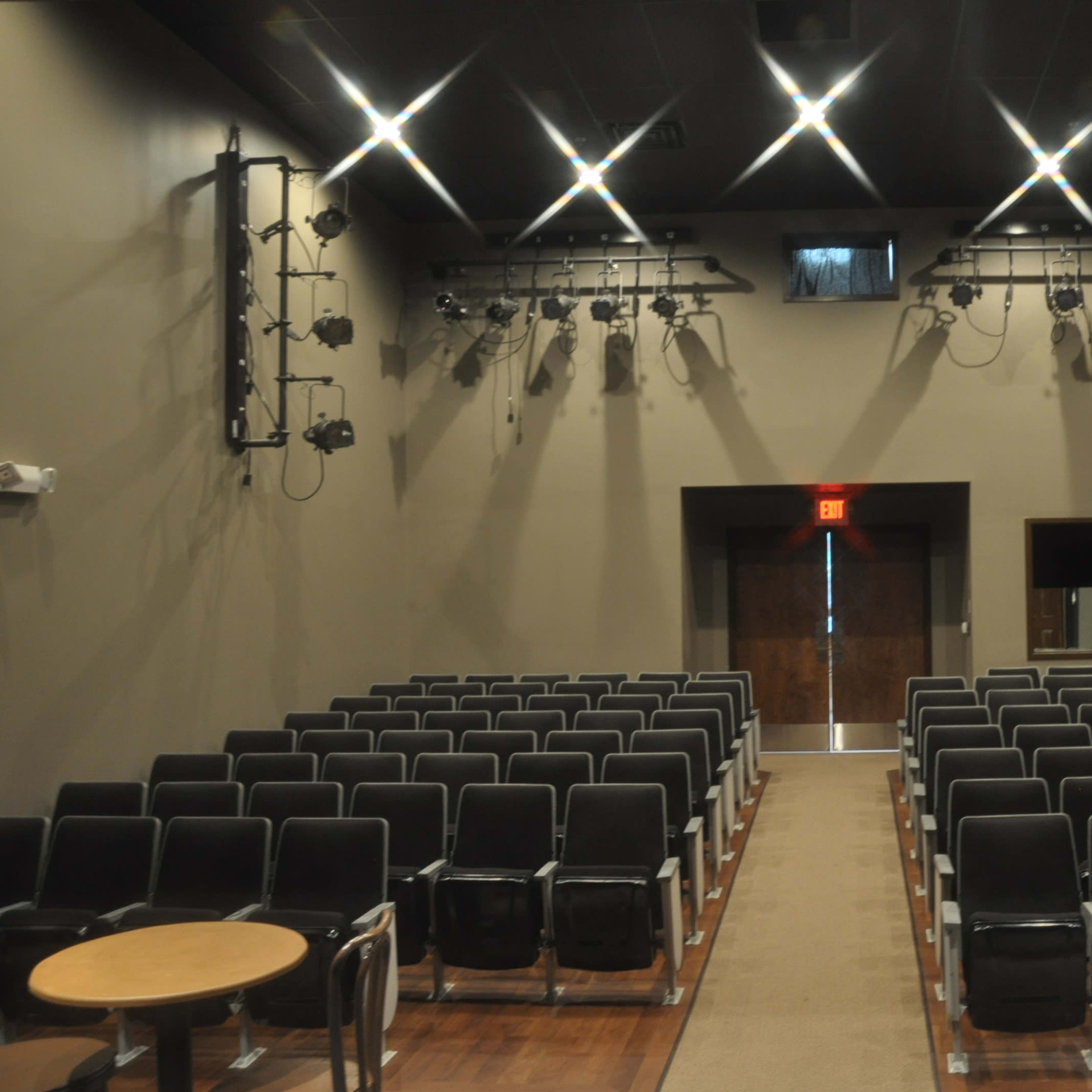 A half-empty theater with rows of black chairs and stage lighting fixtures mounted on the walls.