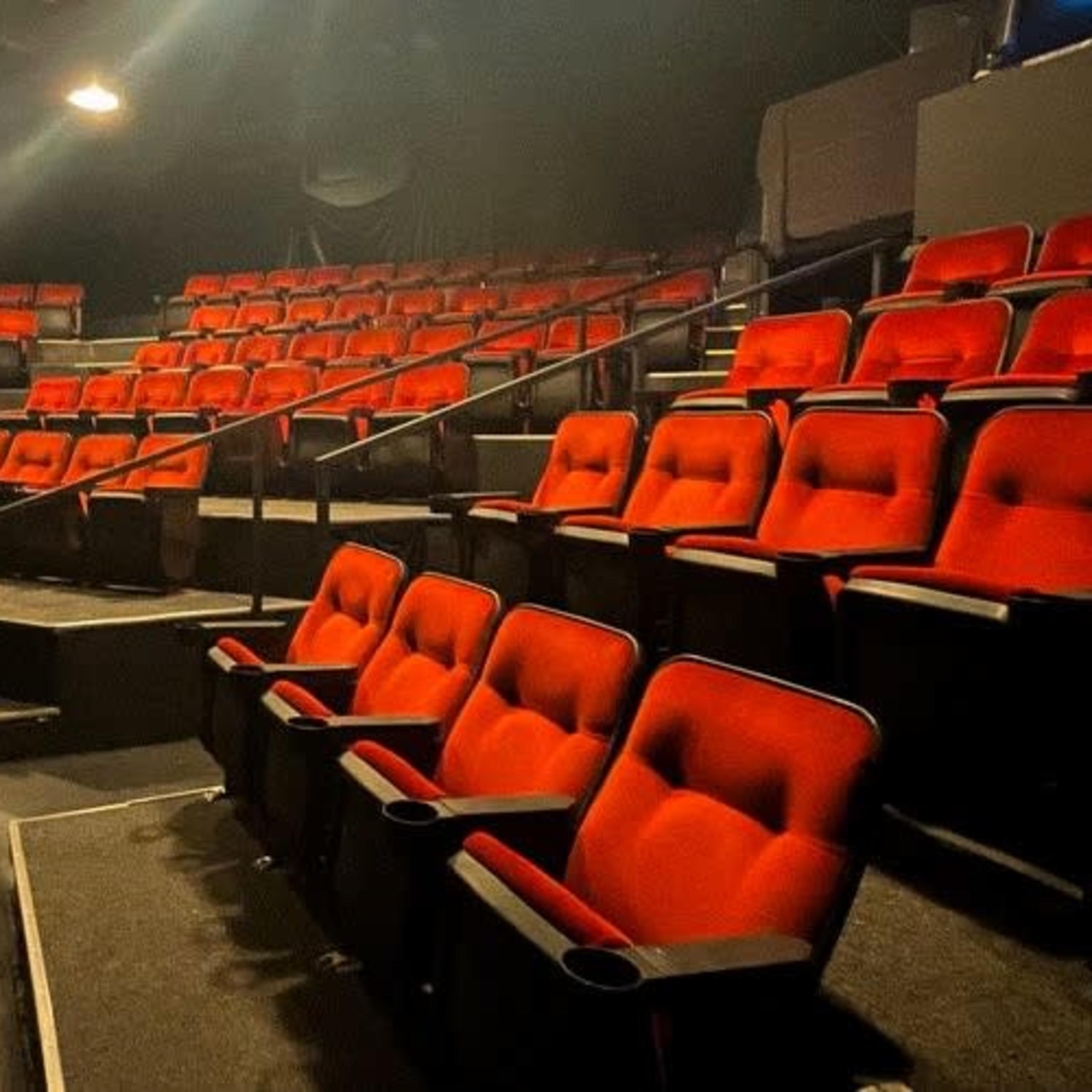 An empty theater with multiple rows of red upholstered seats arranged in a staggered fashion.