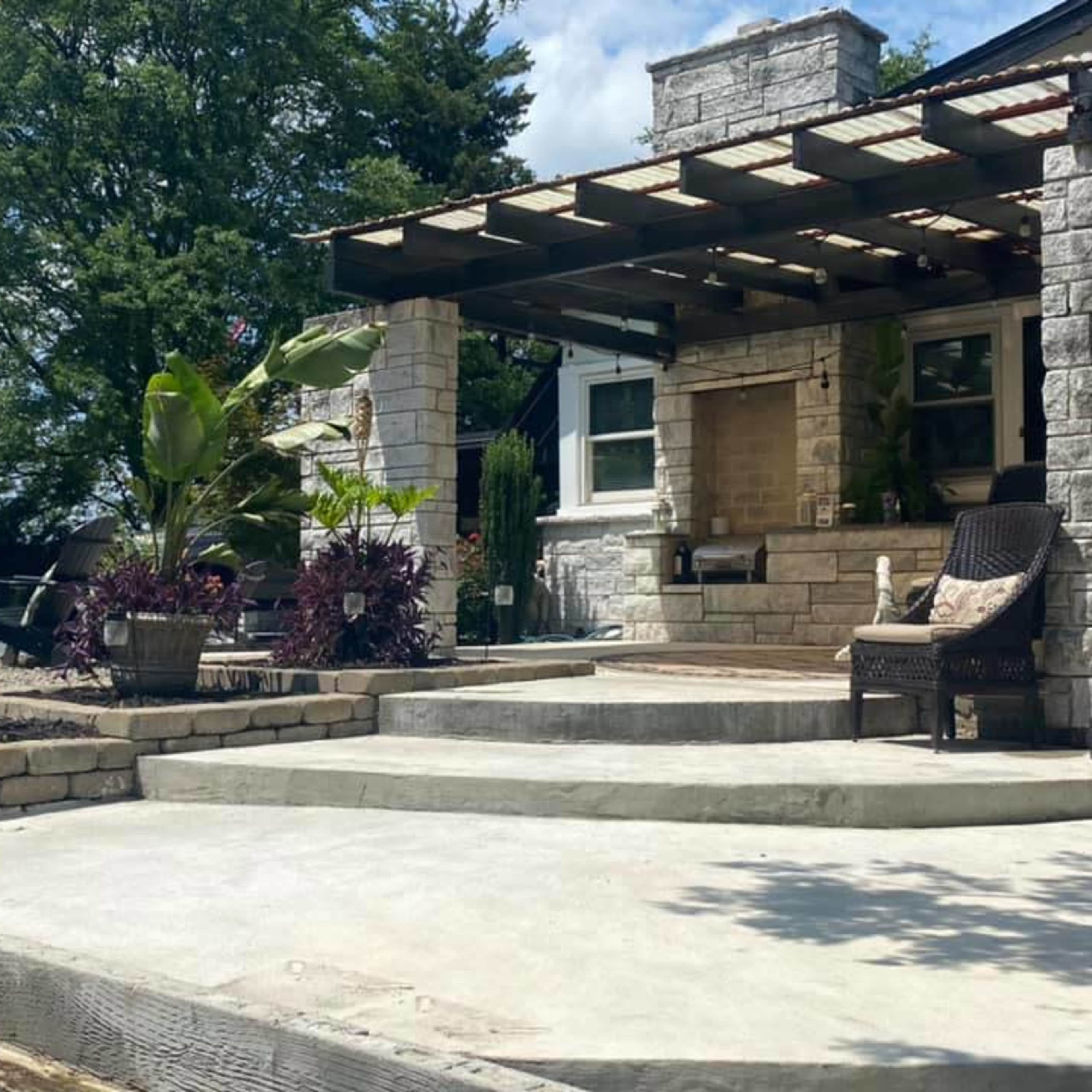 A stone house features a front porch with steps, surrounded by potted plants and a landscaped area.