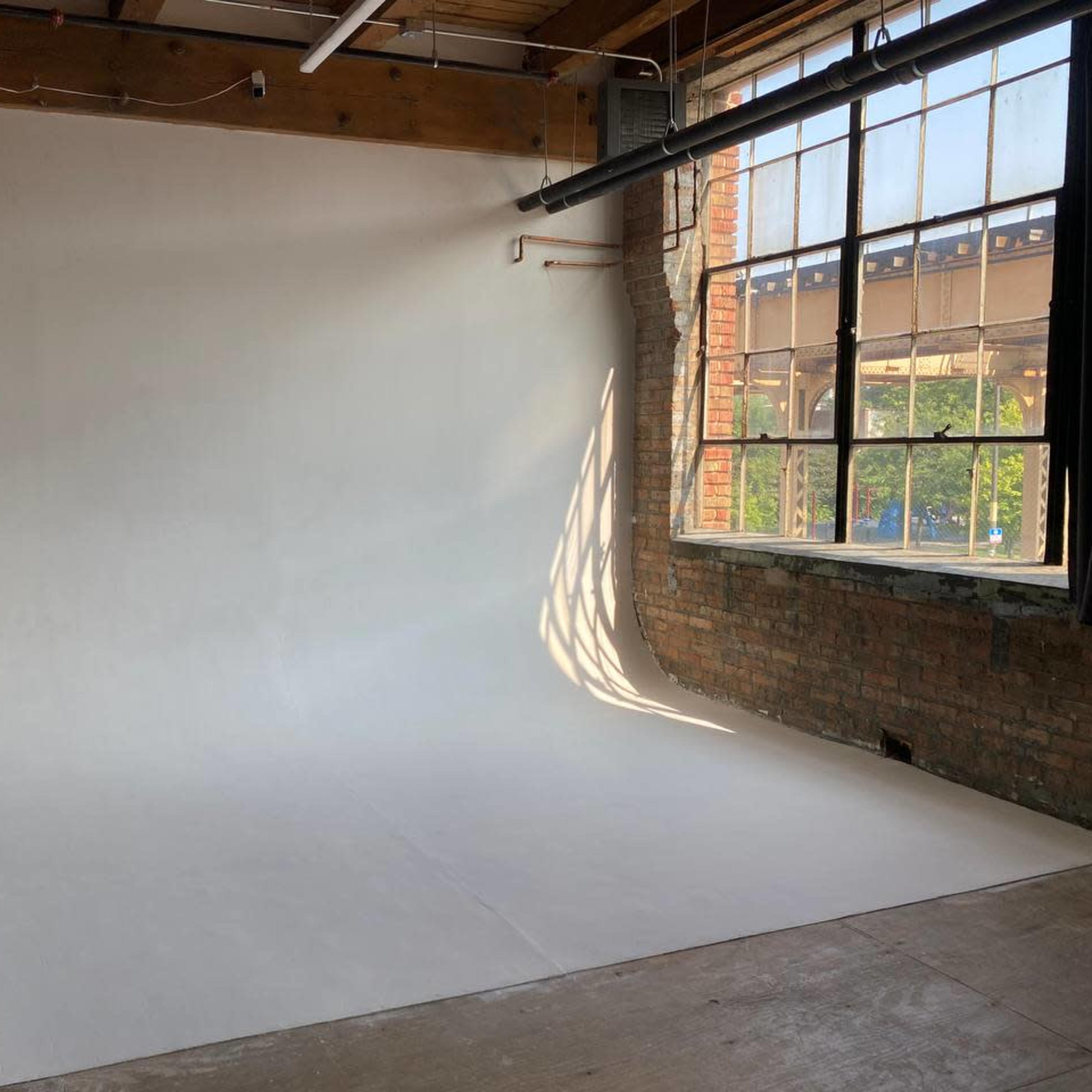 A spacious photography studio with a white backdrop and a large window allowing natural light to enter.